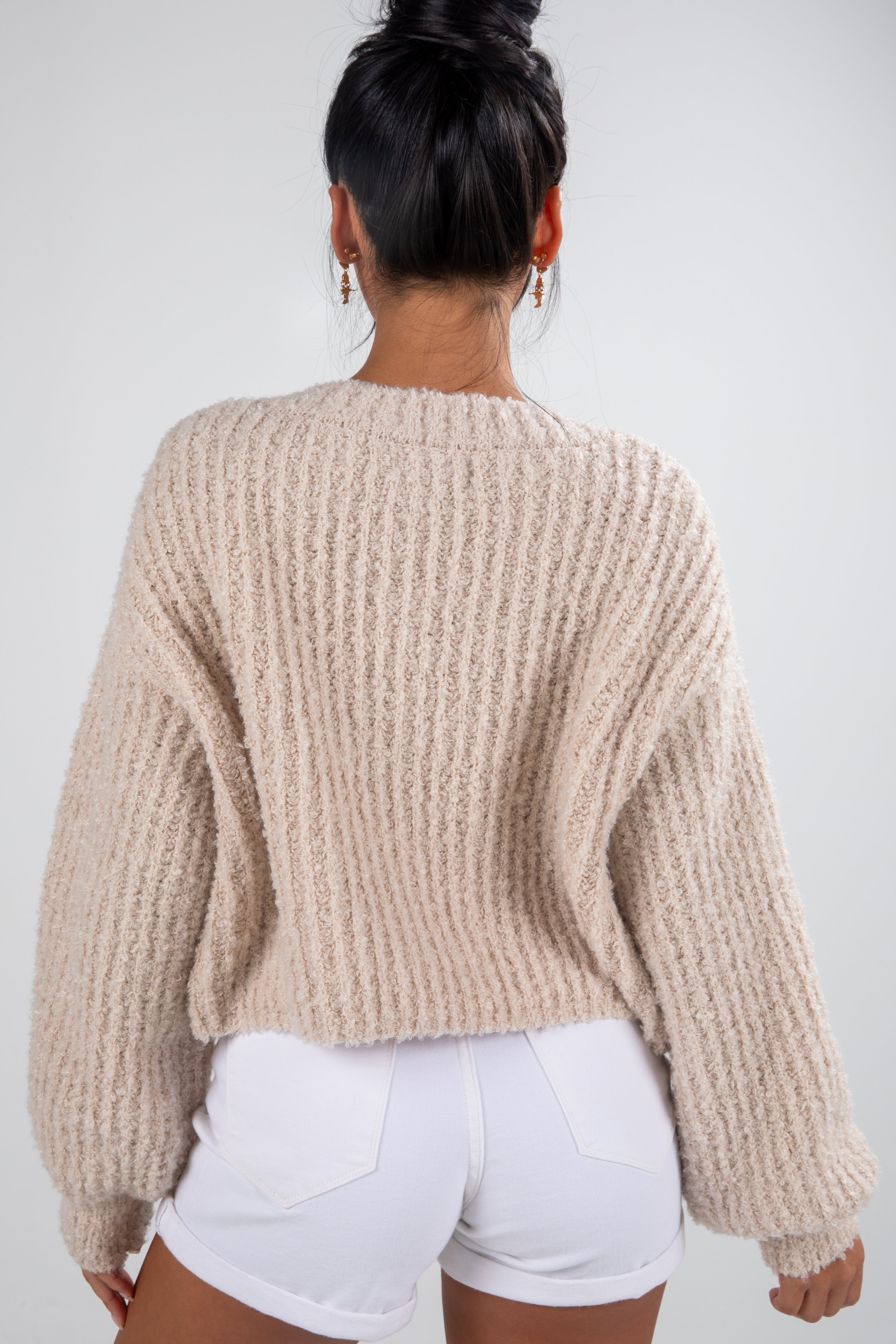 Person wearing a beige chunky knit sweater and white shorts on a plain background