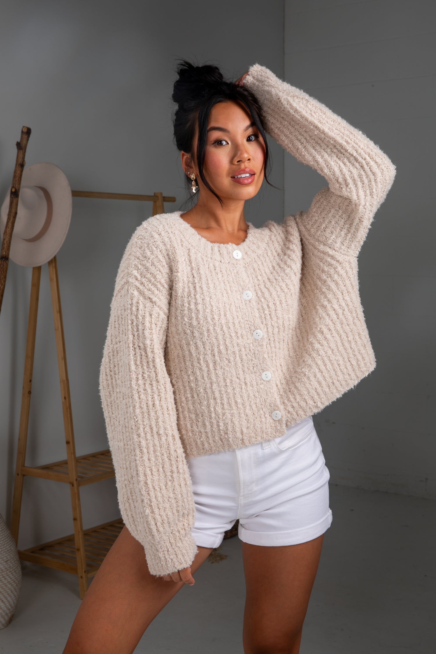 Woman wearing a beige knitted cardigan and white shorts in a minimalistic setting.