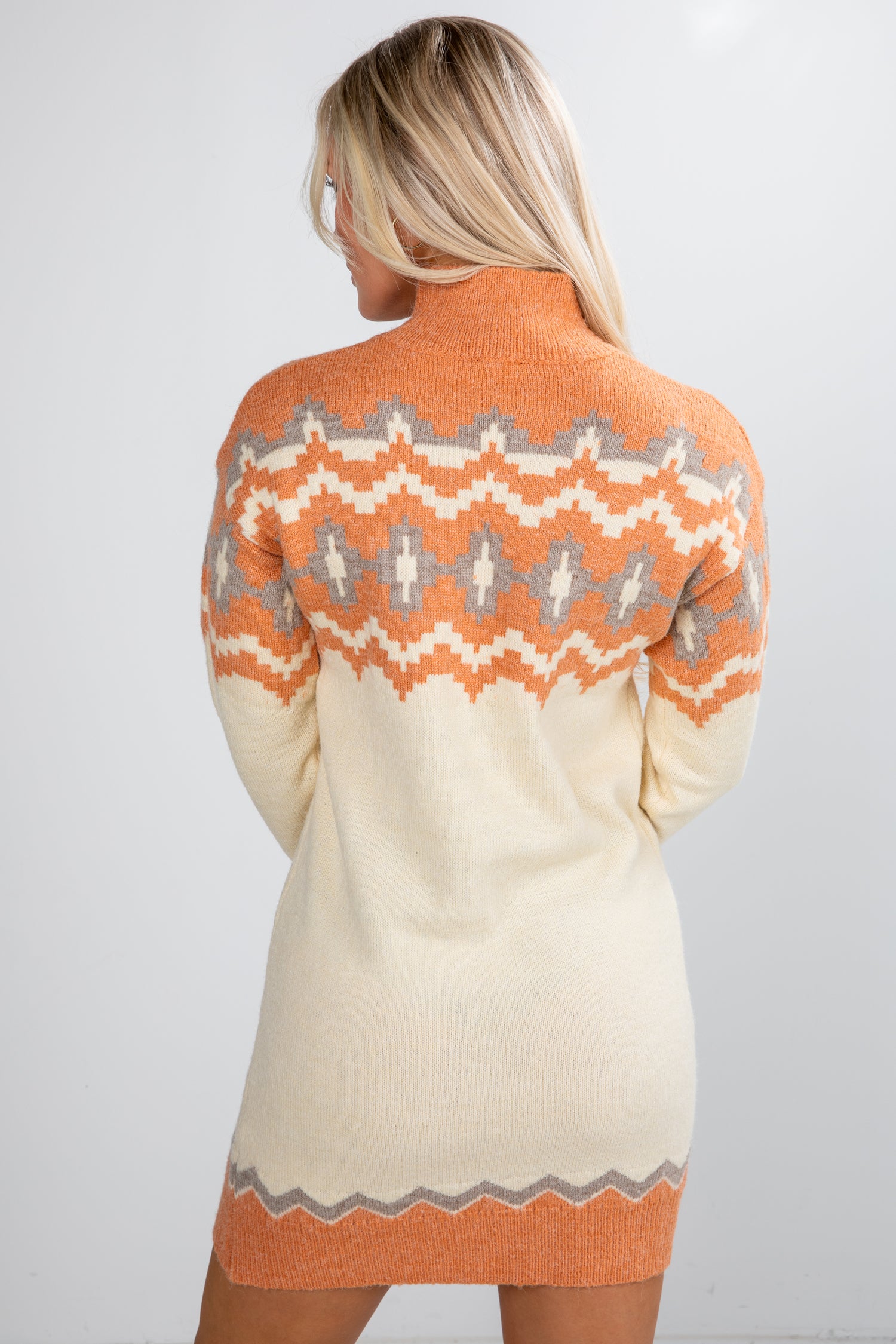 Woman wearing a cream and orange patterned sweater dress on a white background