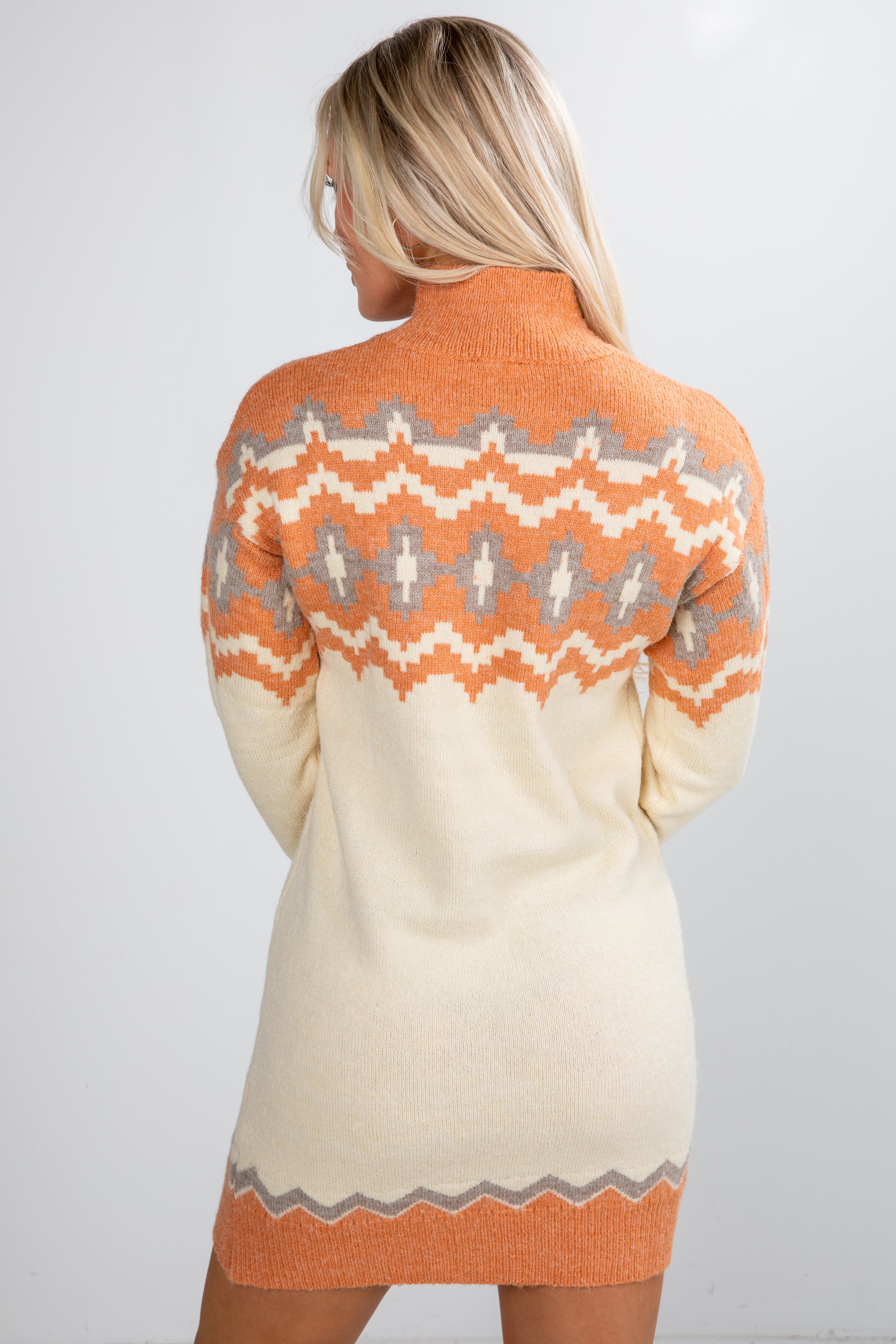 Woman wearing a cream and orange patterned sweater dress on a white background