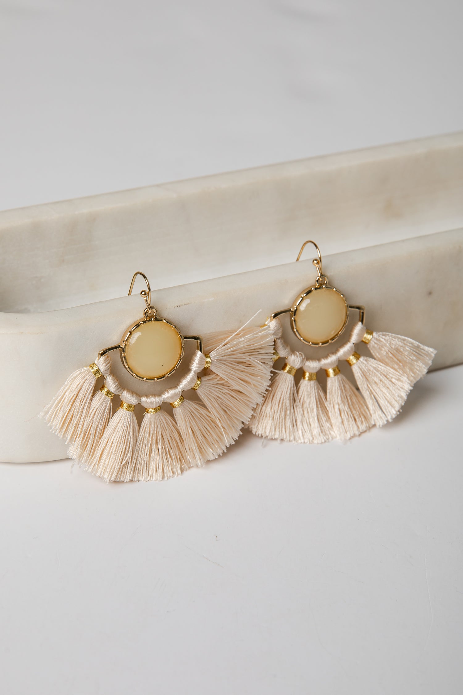 Pair of gold-framed earrings with tassels on a light surface