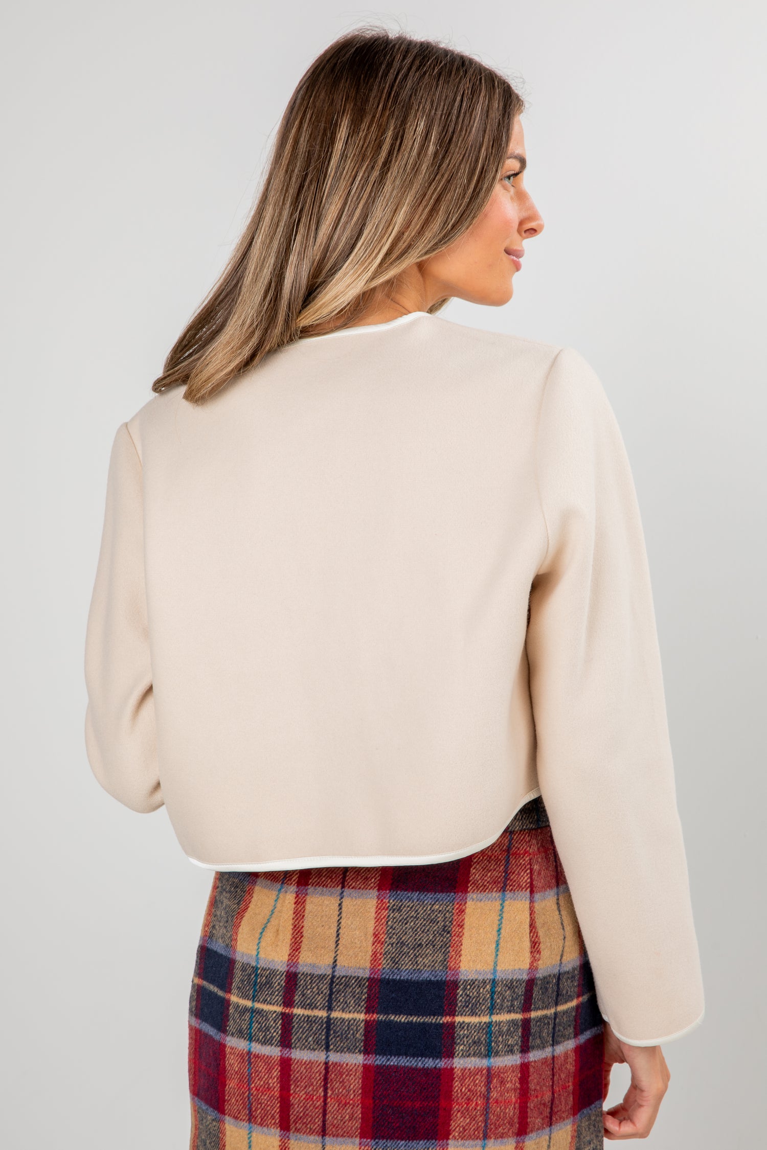 Woman wearing a beige sweater and plaid skirt on a plain background