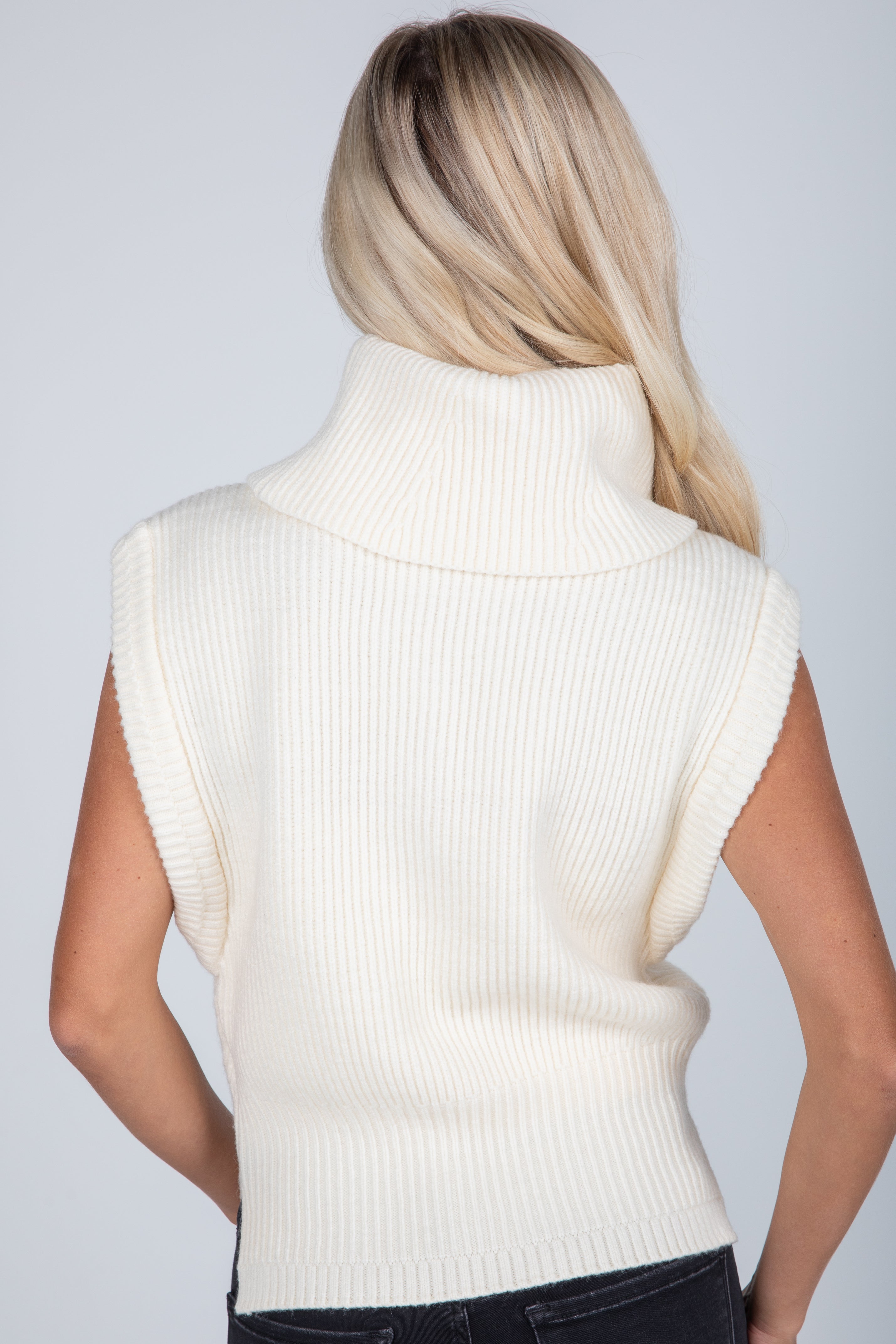 Person wearing a white sleeveless sweater against a plain background
