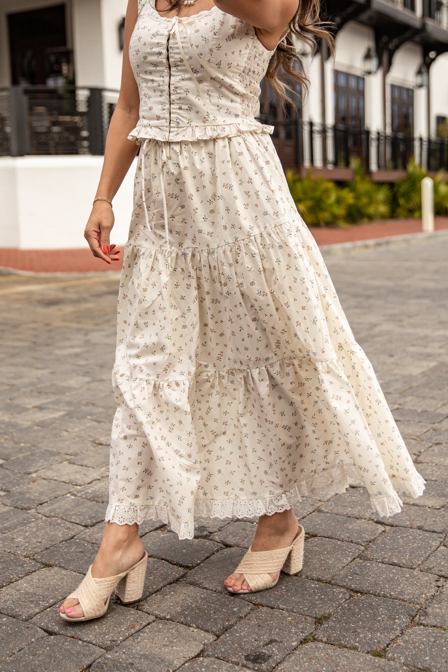 Woman wearing a white floral dress on a paved street.