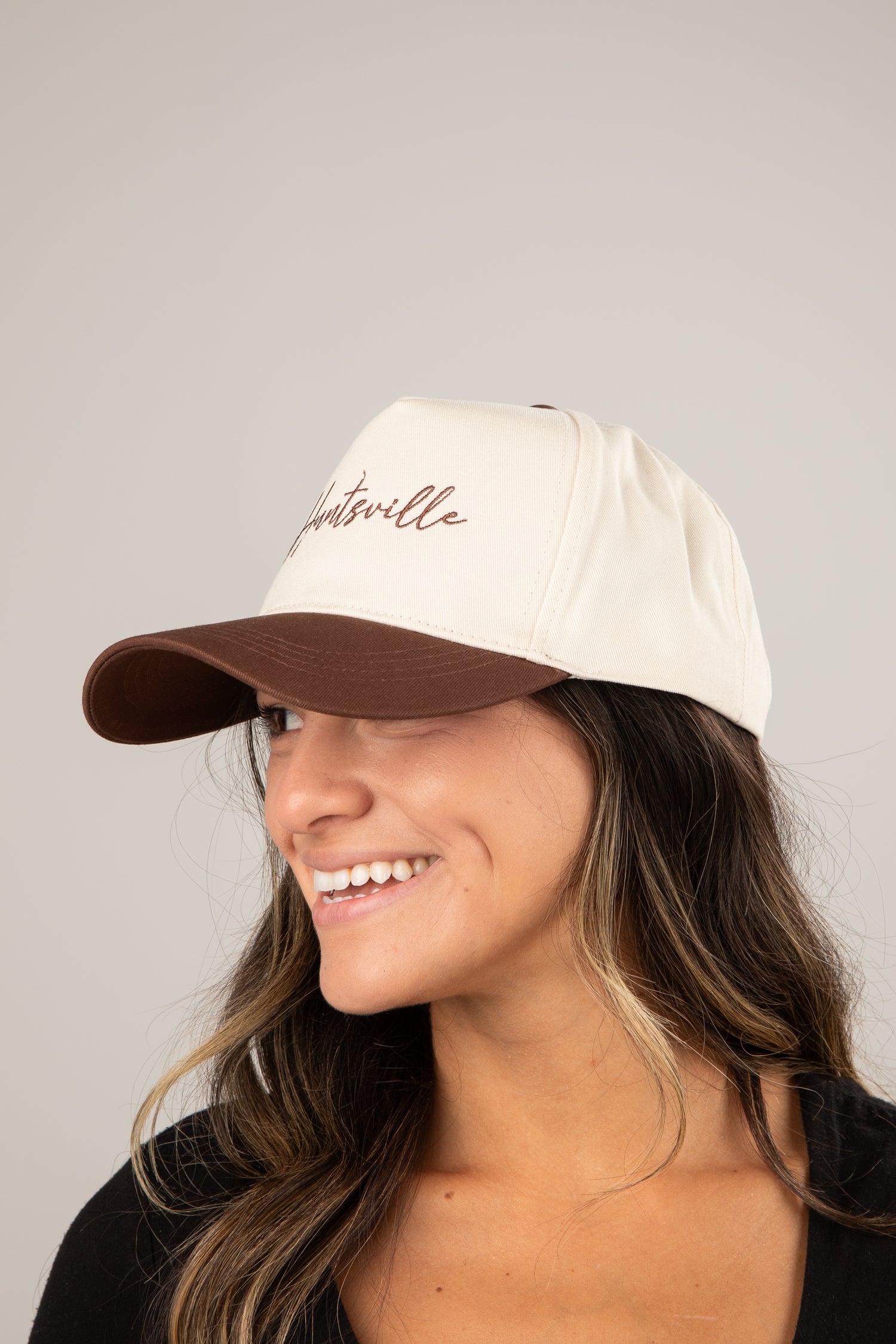 Woman wearing a beige cap with brown brim and embroidered text on a plain background