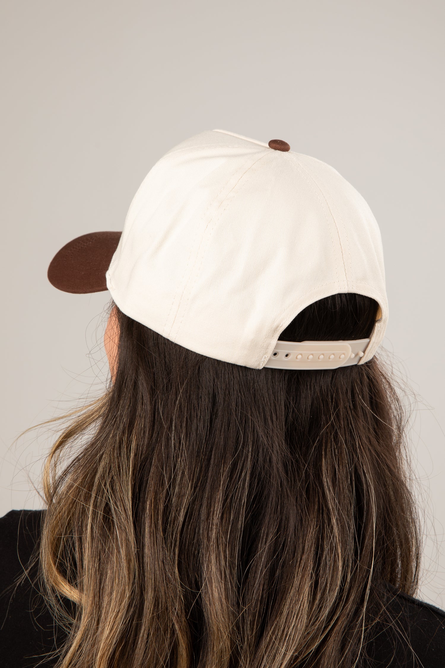 Person wearing a white cap with a brown brim on a plain background