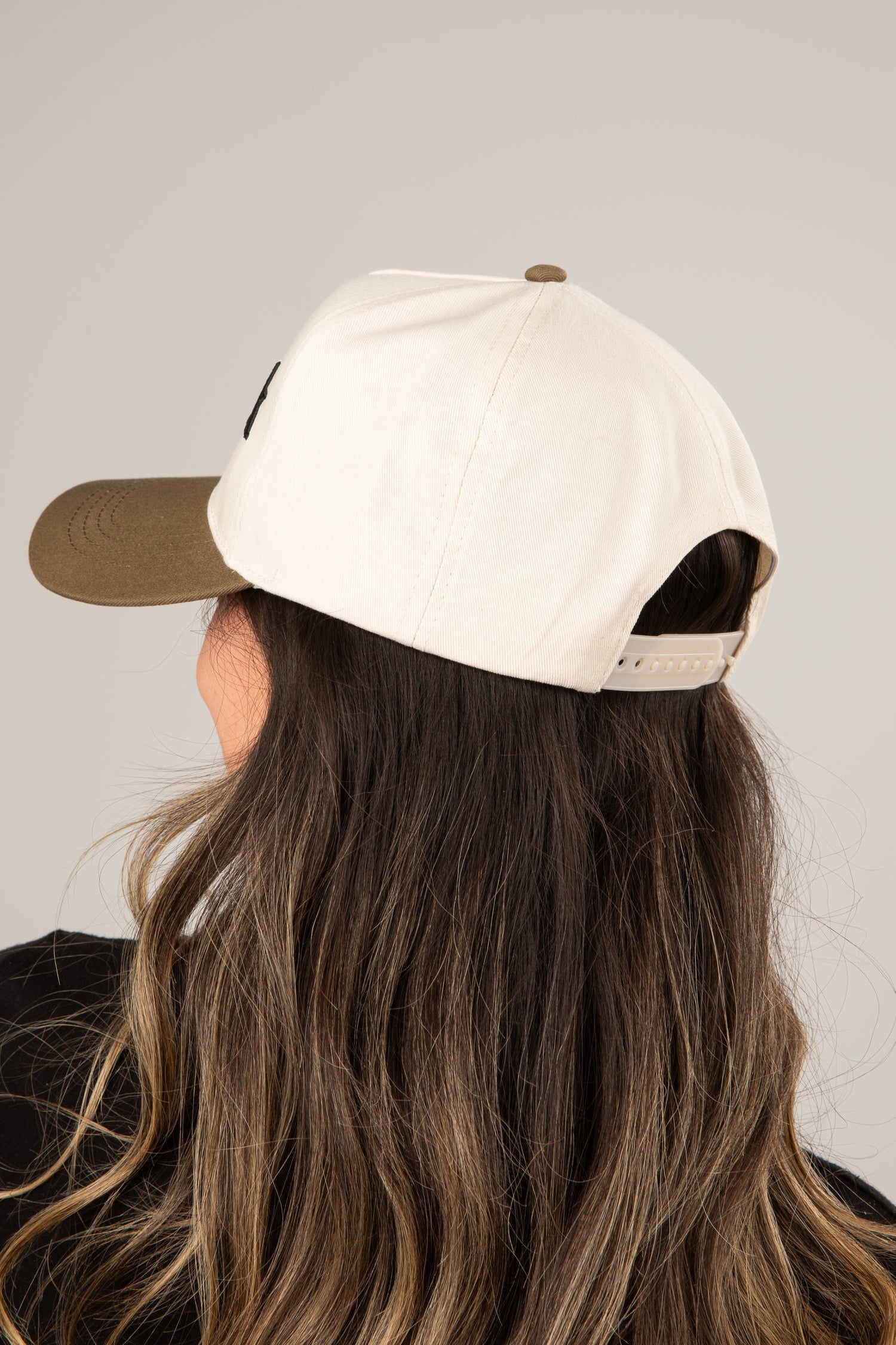 Person wearing a beige cap with a brown bill on a plain background