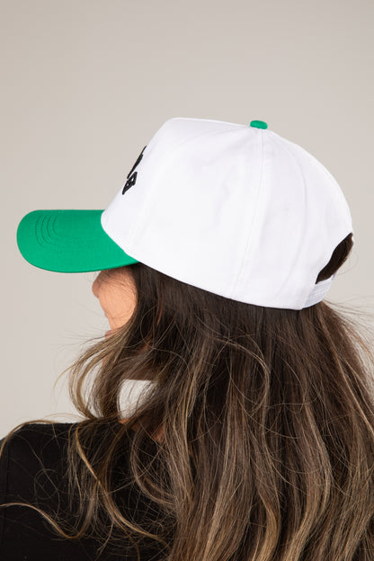 Person wearing a white cap with green brim and back on a neutral background