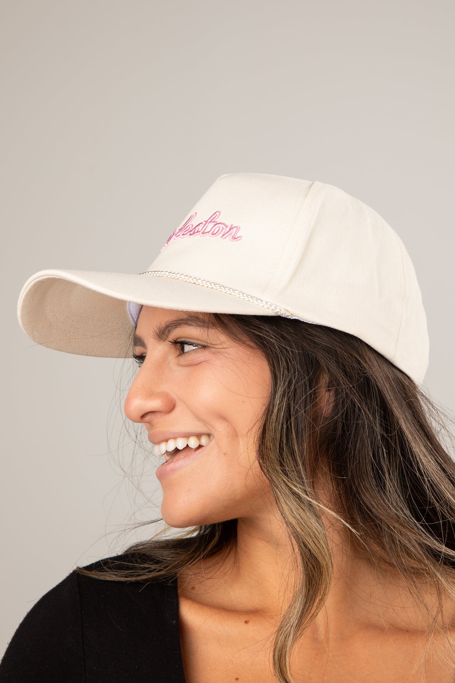 Woman wearing a beige cap with pink text on a gray background