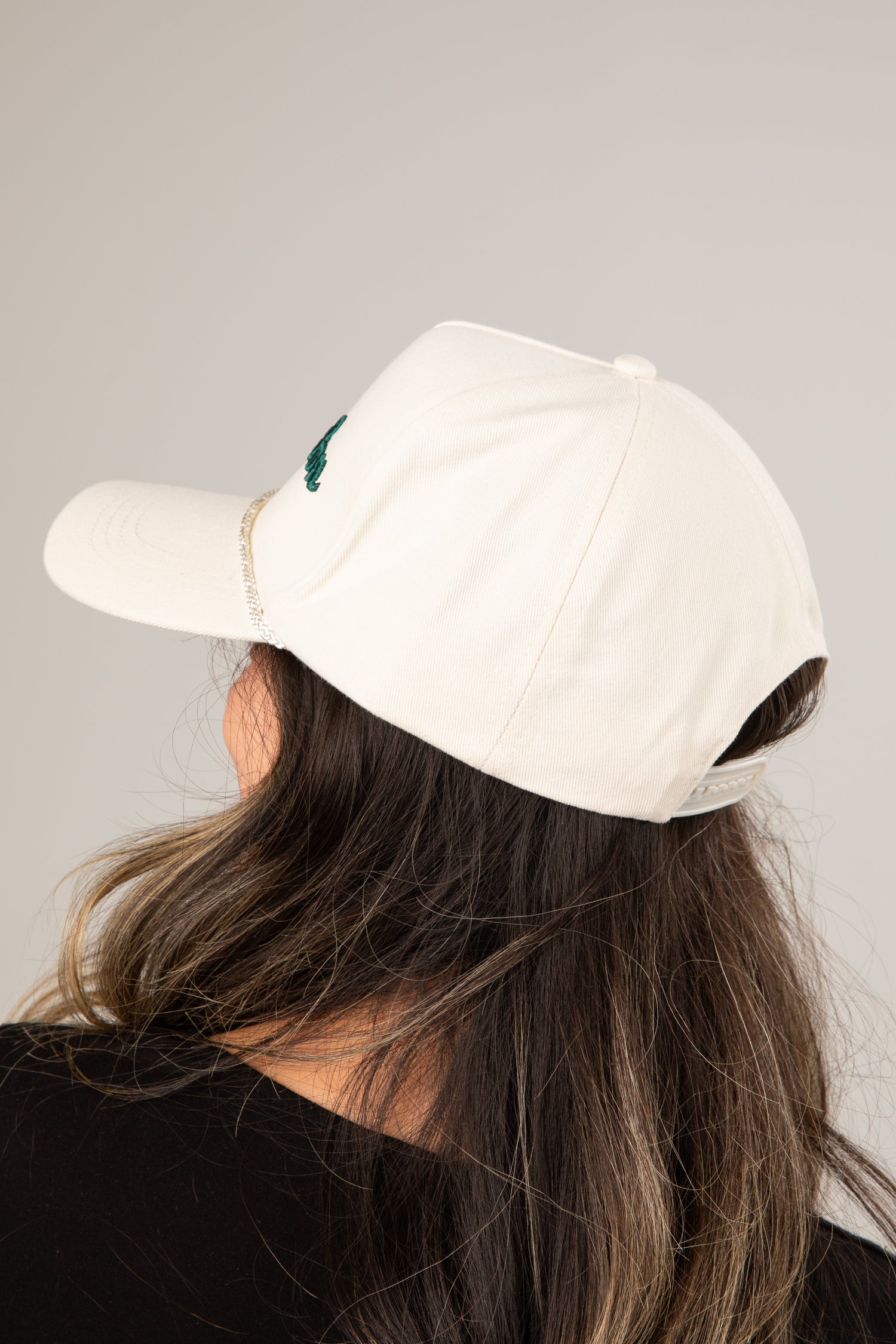 Person wearing a white cap with a logo on a plain background