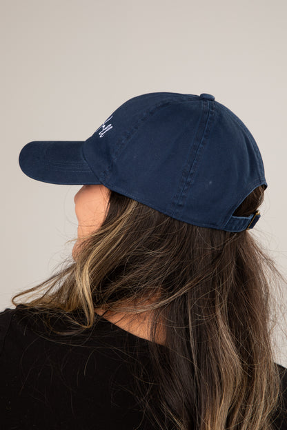 Person wearing a navy blue cap with a logo on a plain background