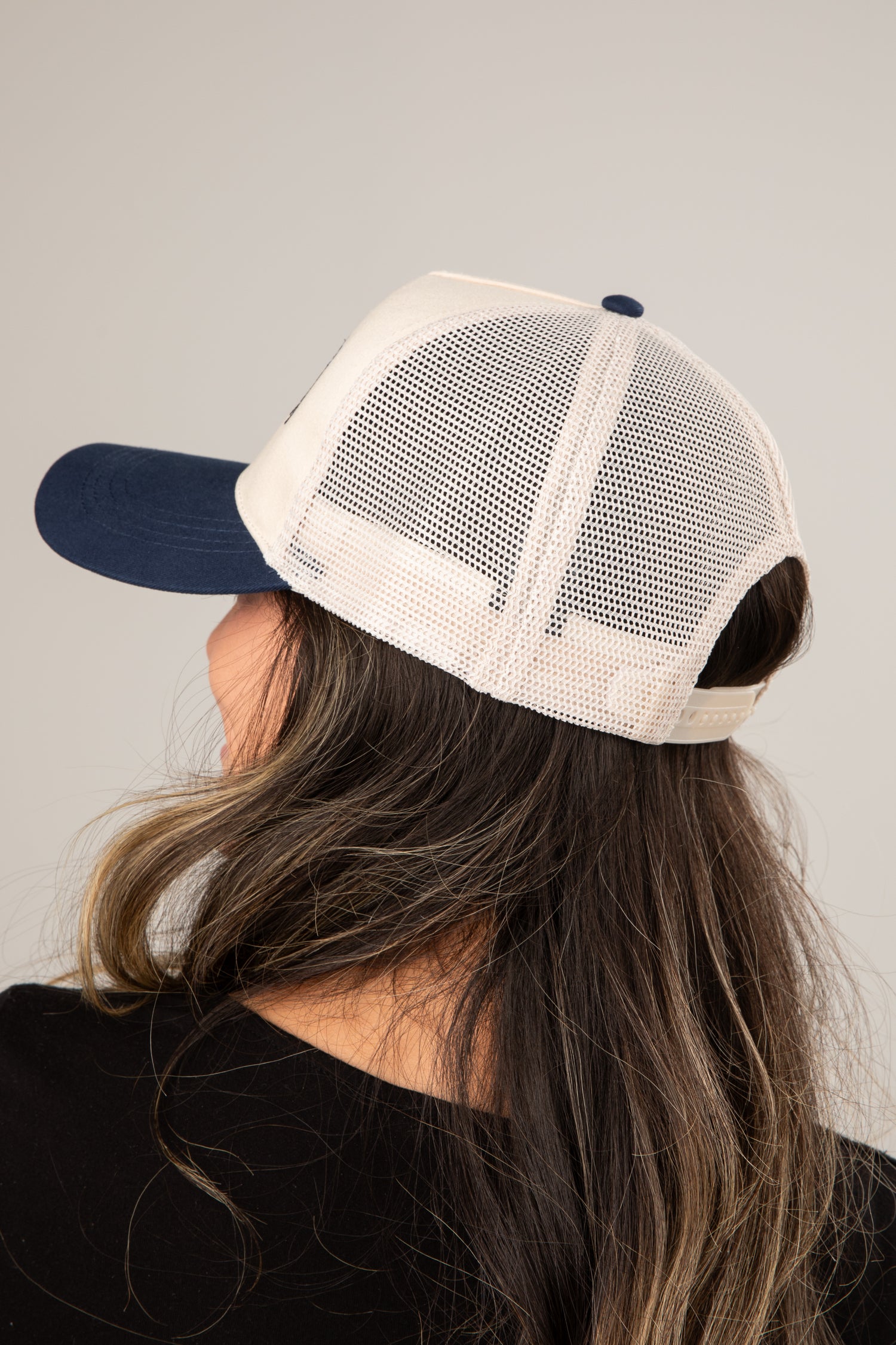 Person wearing a beige and navy trucker hat on a plain background