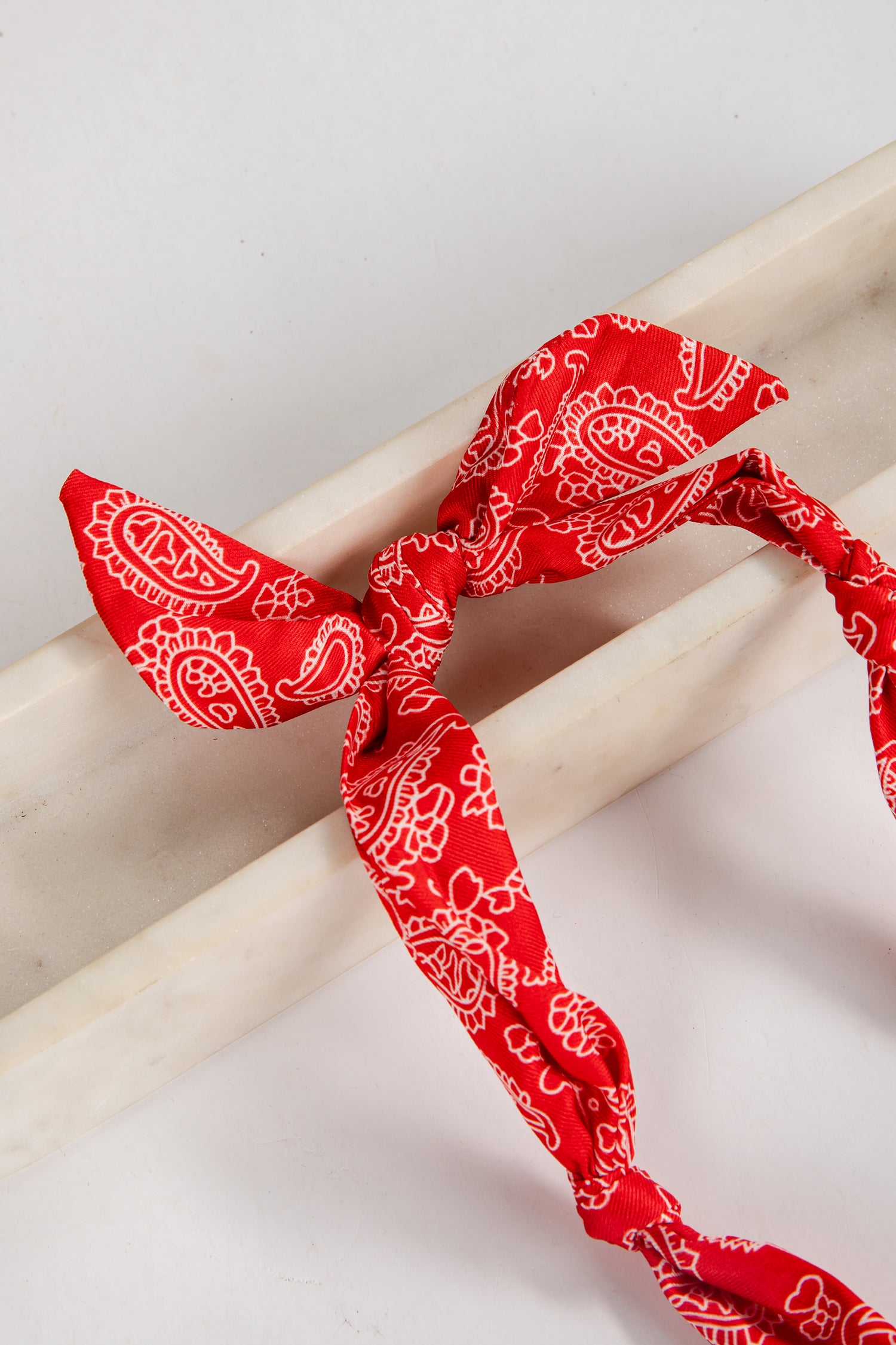 Red bandana with white patterns tied around a wooden stick on a light background