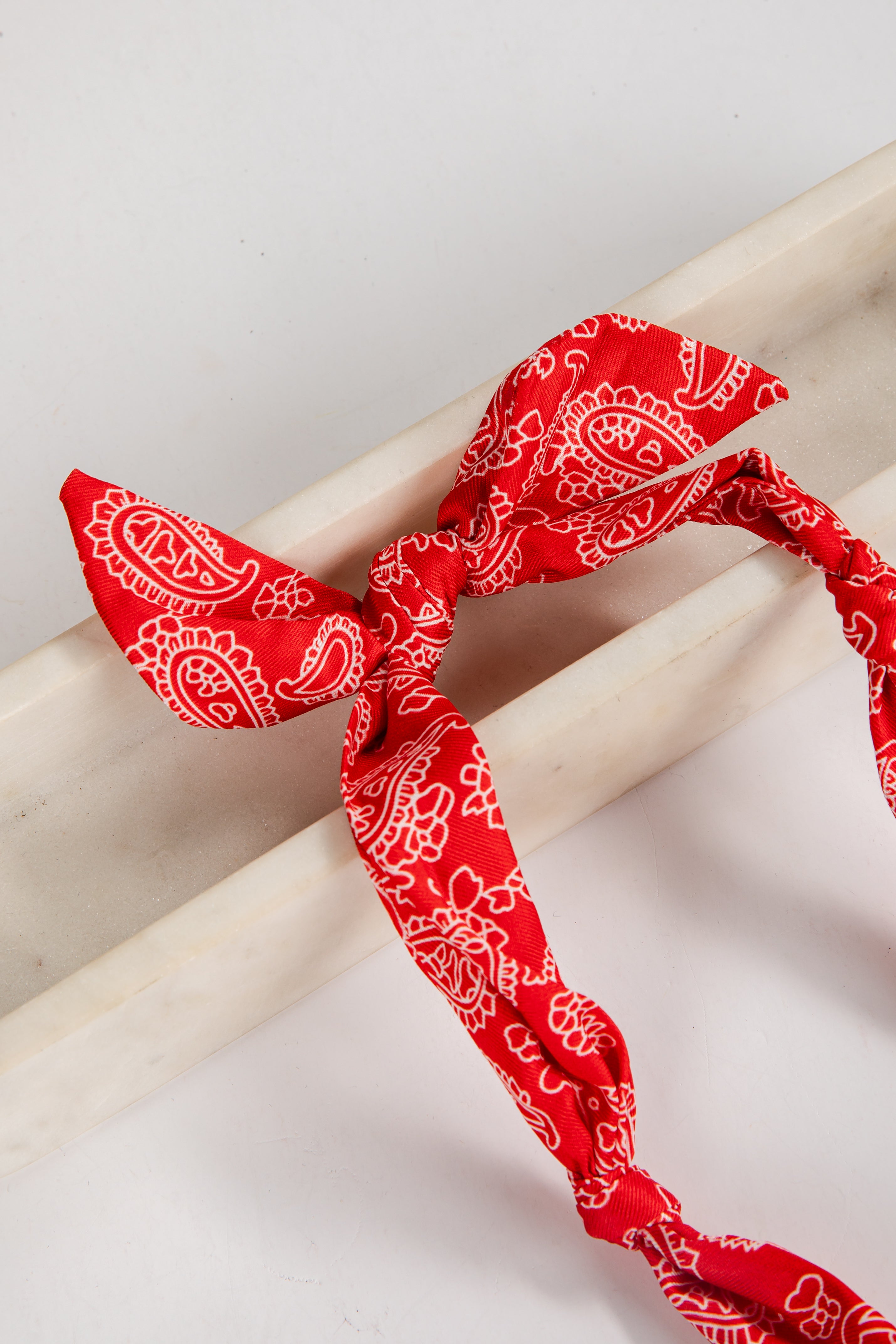 Red bandana with white patterns tied around a wooden stick on a light background
