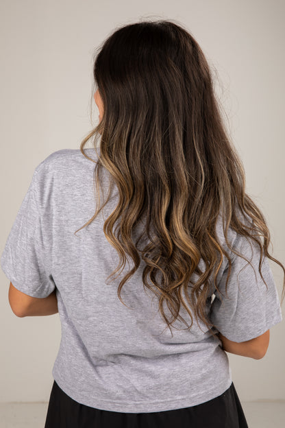 Person wearing a gray t-shirt with long, wavy hair on a plain background