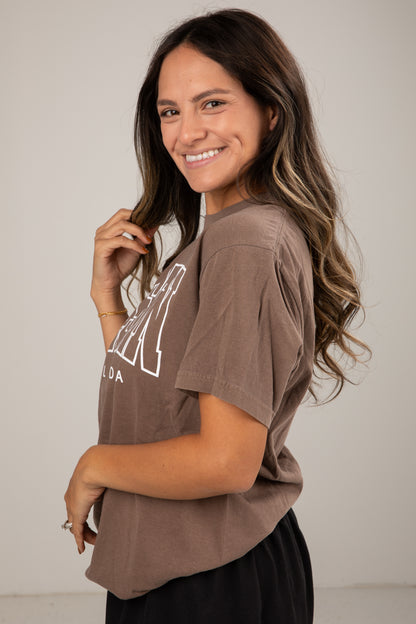 Woman wearing a brown t-shirt with a graphic design on a plain background