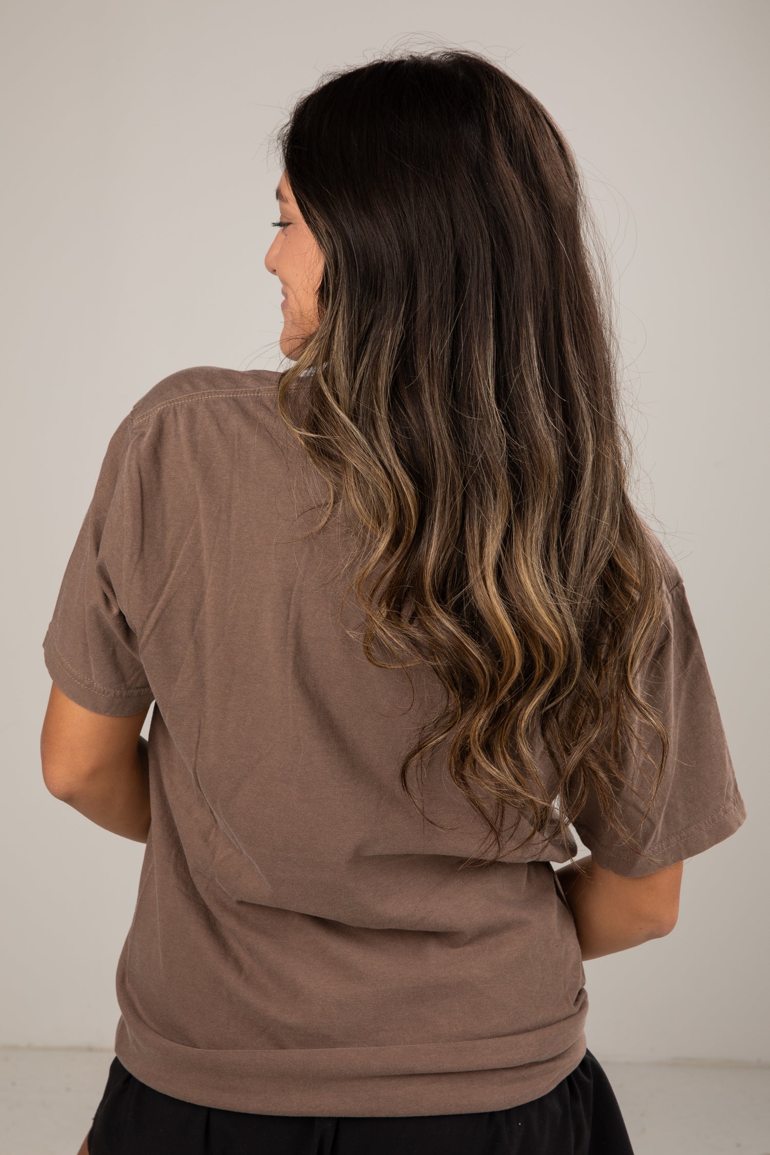 Woman wearing a brown shirt with long, wavy hair on a plain background