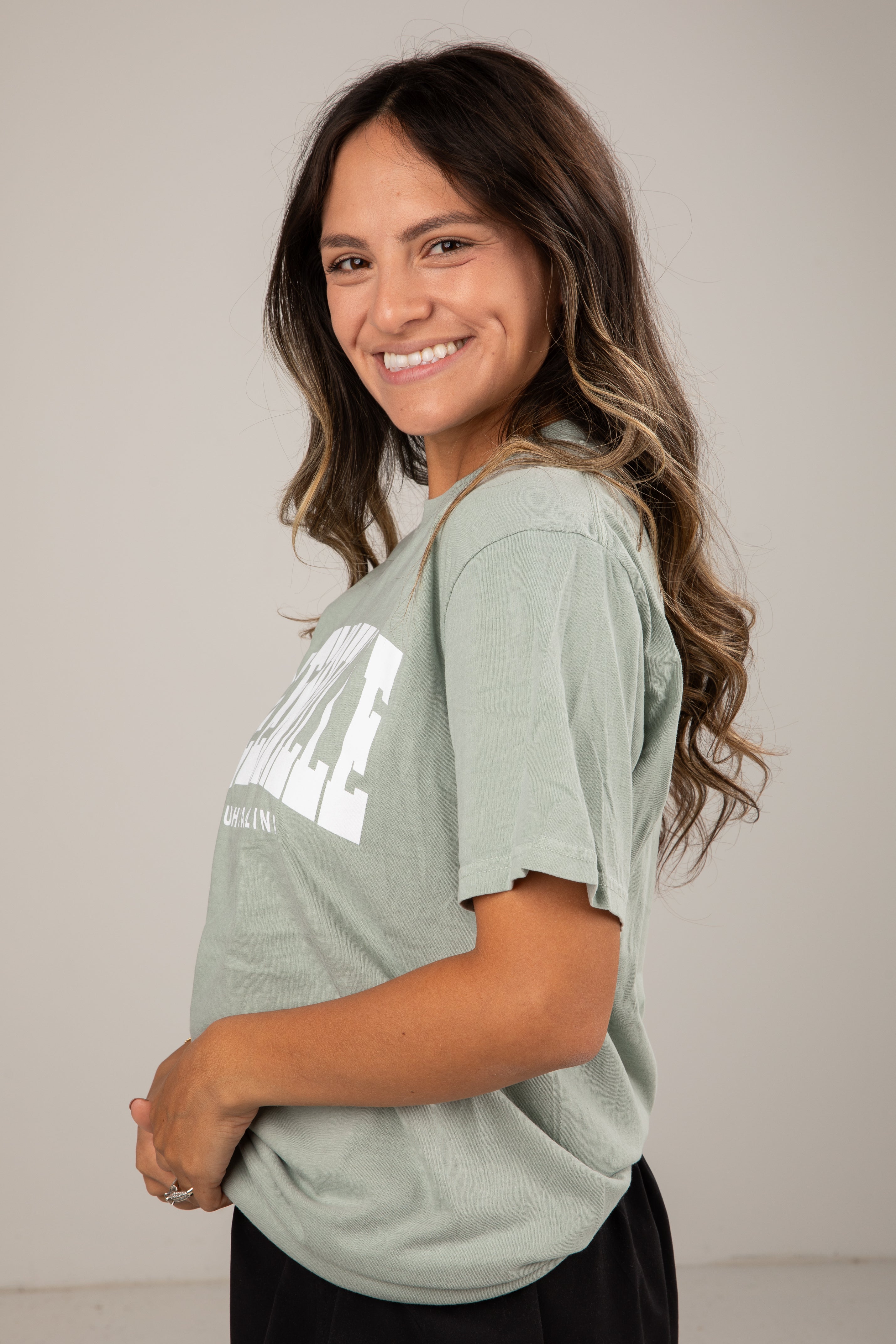 Woman wearing a light green t-shirt with text, standing against a plain background