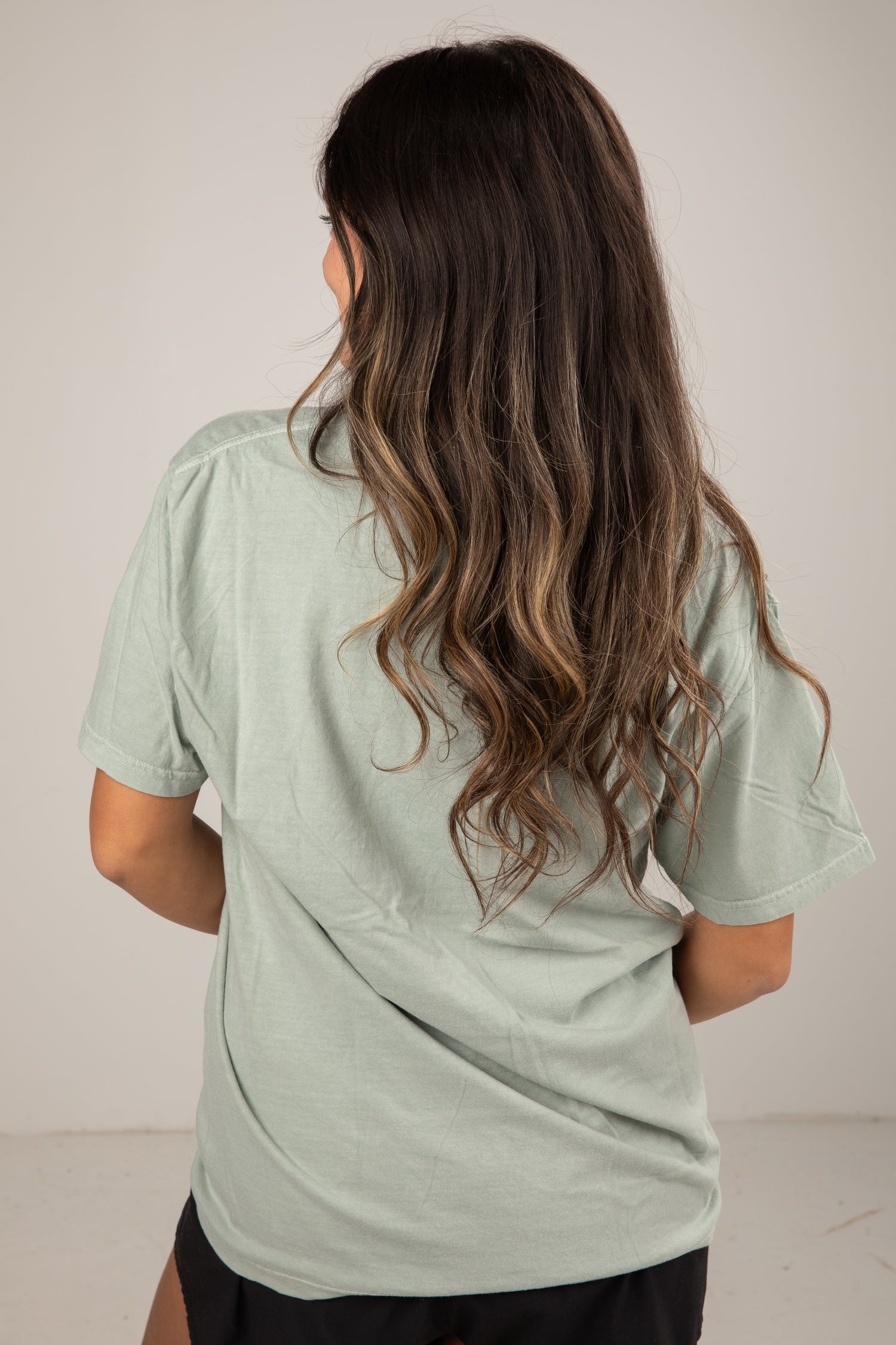 Person wearing a light green t-shirt with long, wavy hair on a plain background