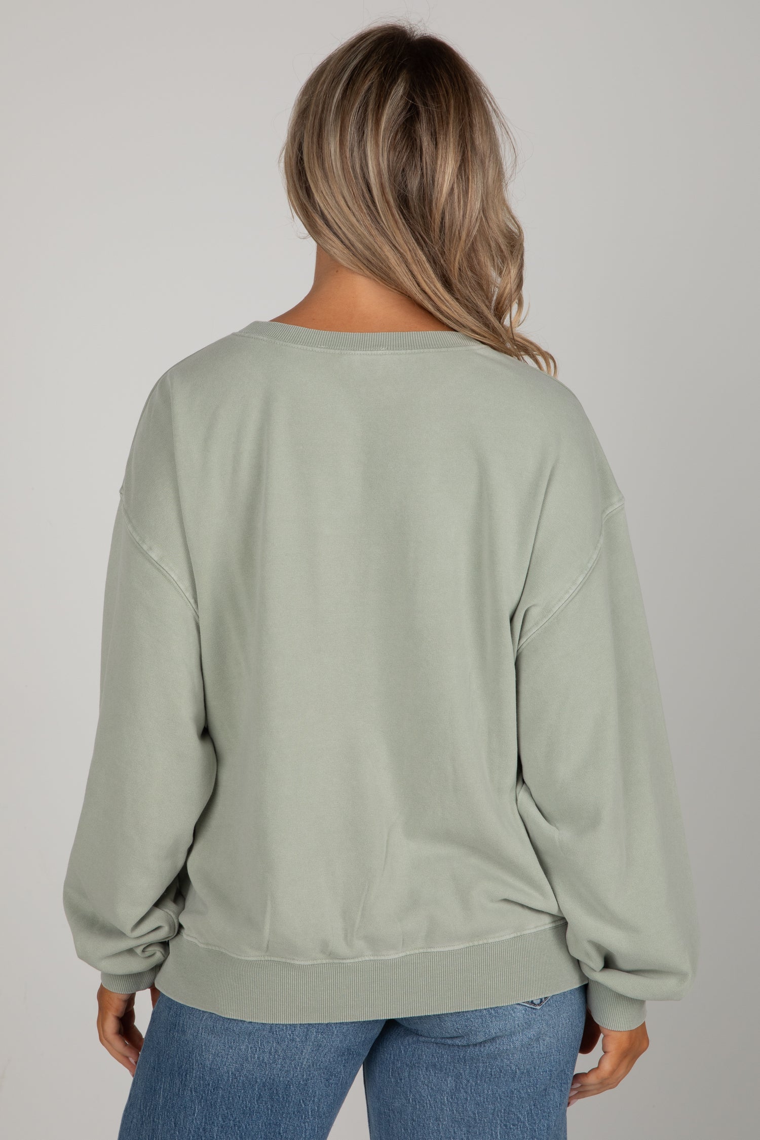 Person wearing a light green sweatshirt and blue jeans on a plain background