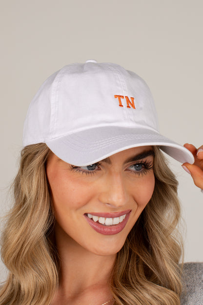 A woman wearing a white baseball cap with orange embroidered &
