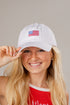 Woman wearing a white cap with an American flag emblem on a plain background
