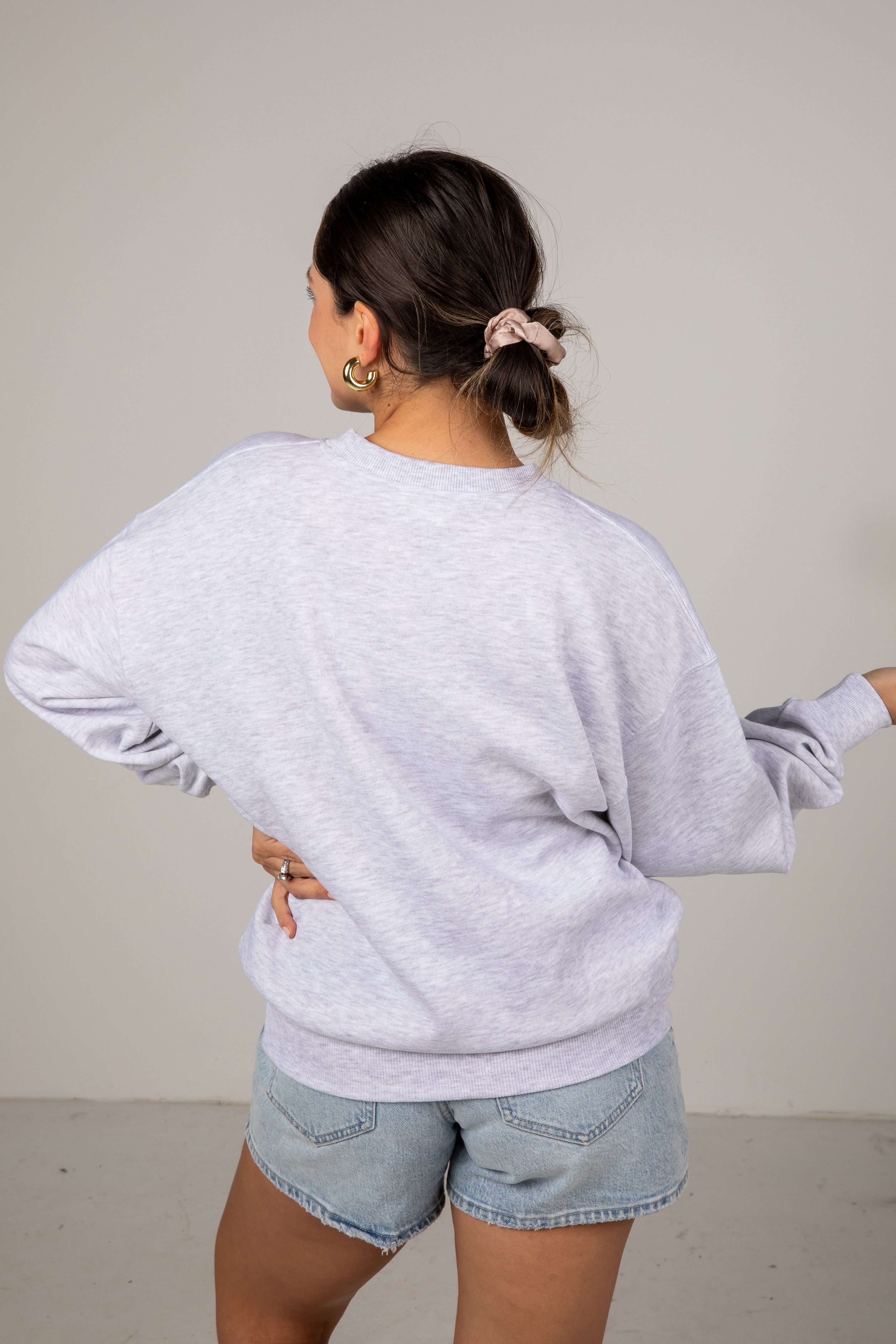 Person wearing a light gray sweatshirt and denim shorts against a plain background