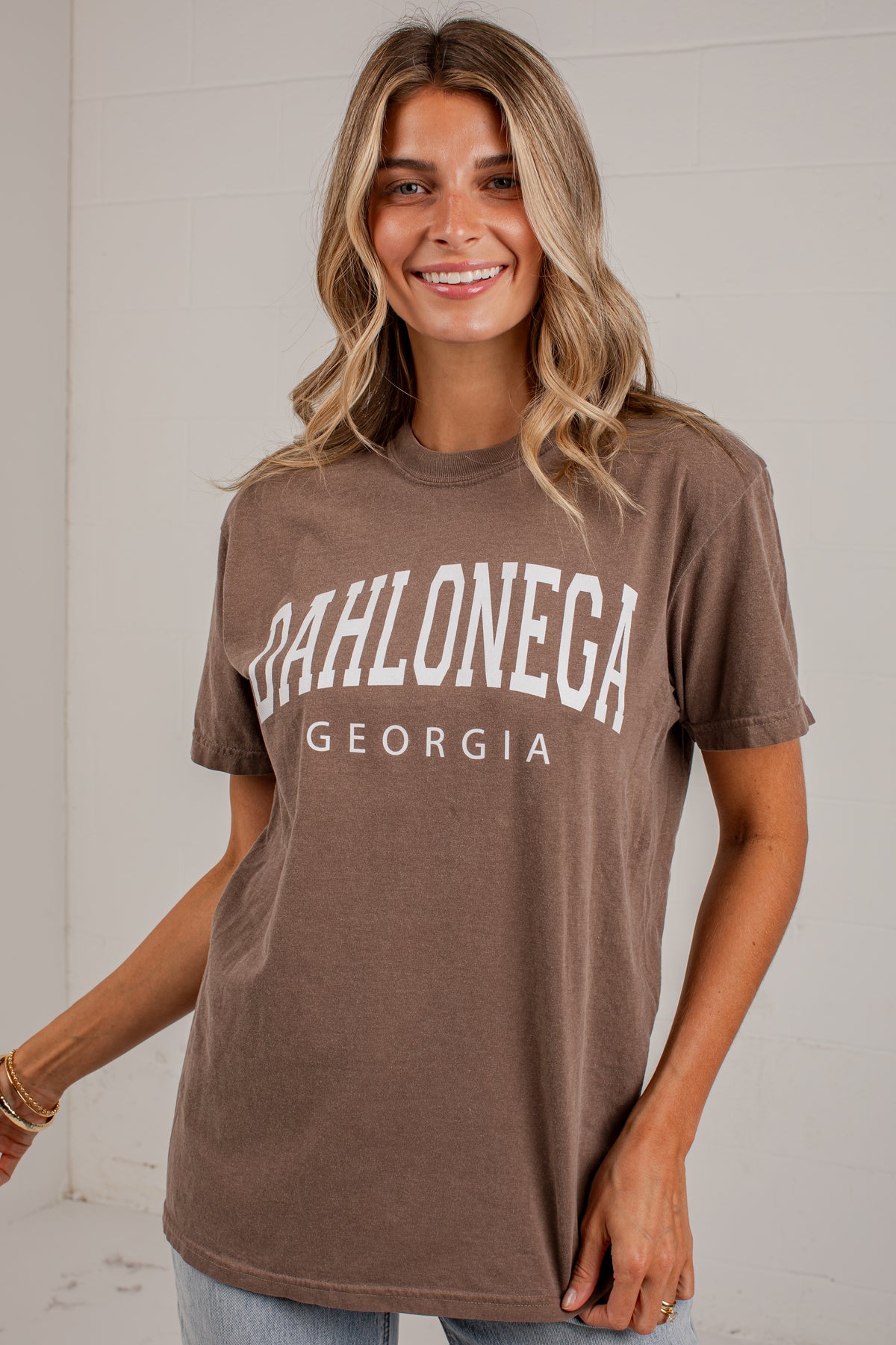 A woman wearing a brown short-sleeve graphic t-shirt with &