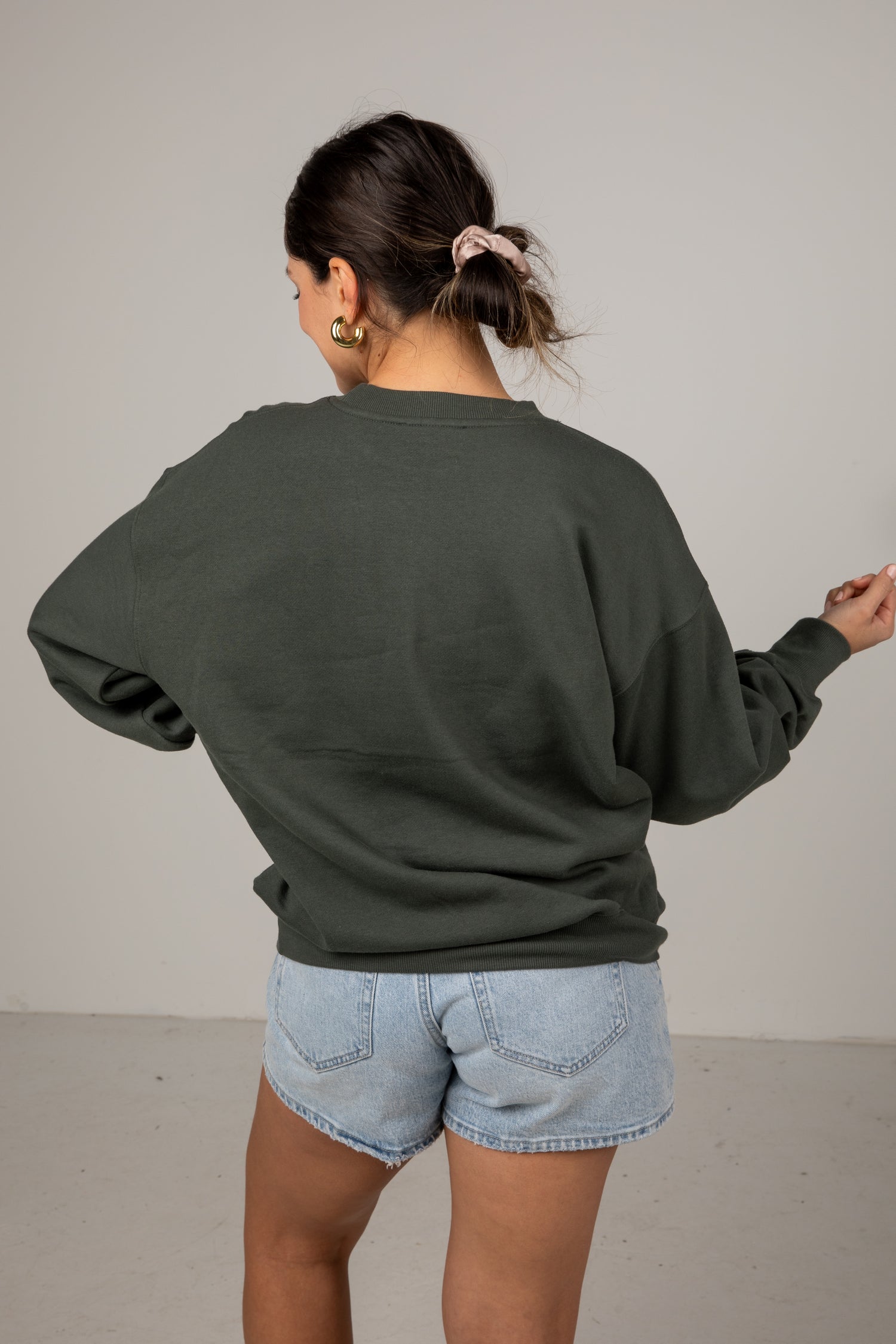 Person wearing a green sweatshirt and light blue shorts against a plain background