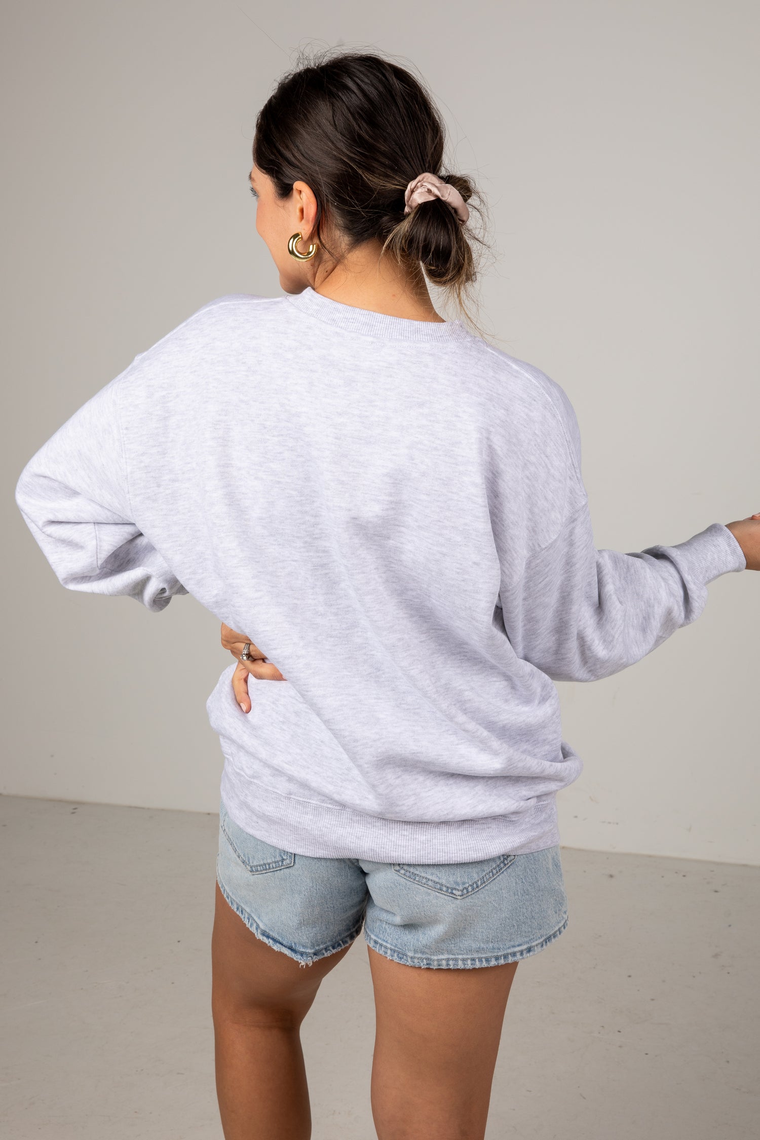 Person wearing a light gray sweatshirt and denim shorts against a plain background