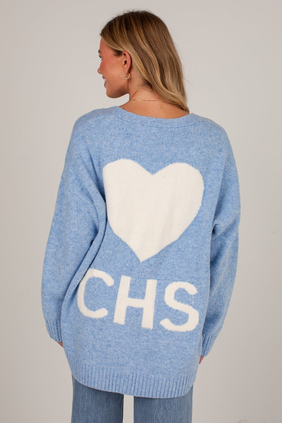 A woman shown from the back wearing a light blue knit sweater with a large white heart and the letters &