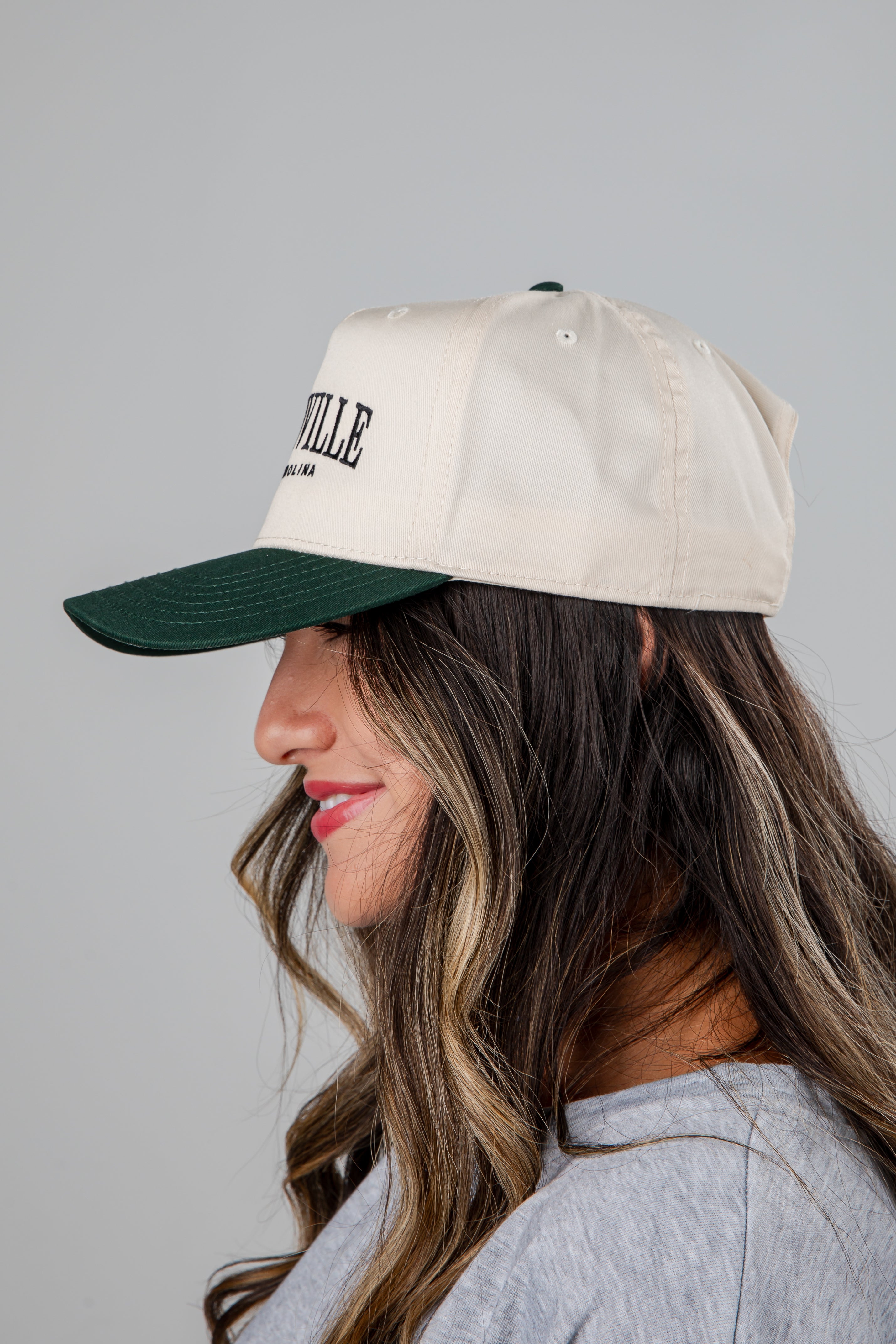 Woman wearing a beige cap with a green bill on a gray background