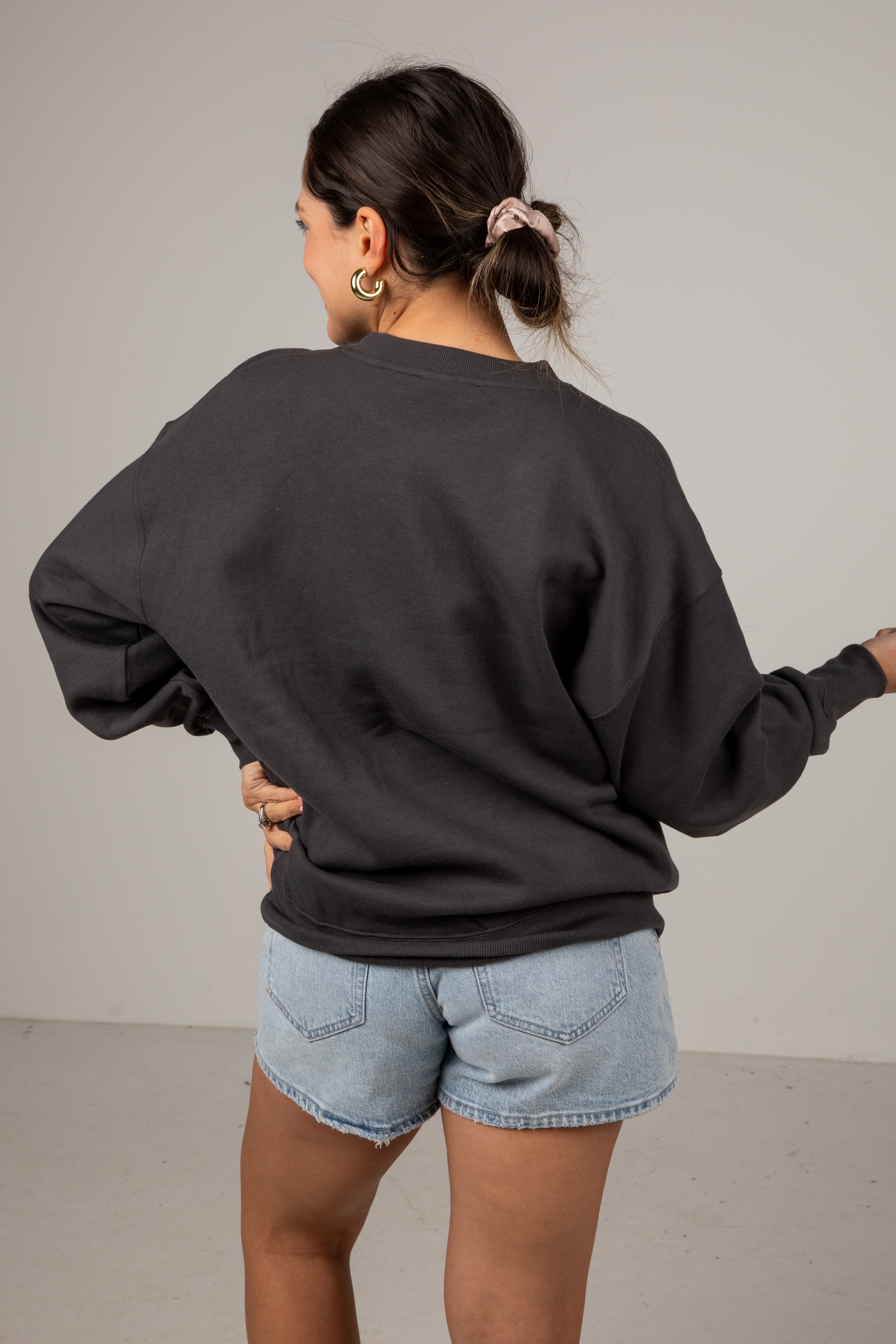 Person wearing a black sweatshirt and denim shorts against a plain background
