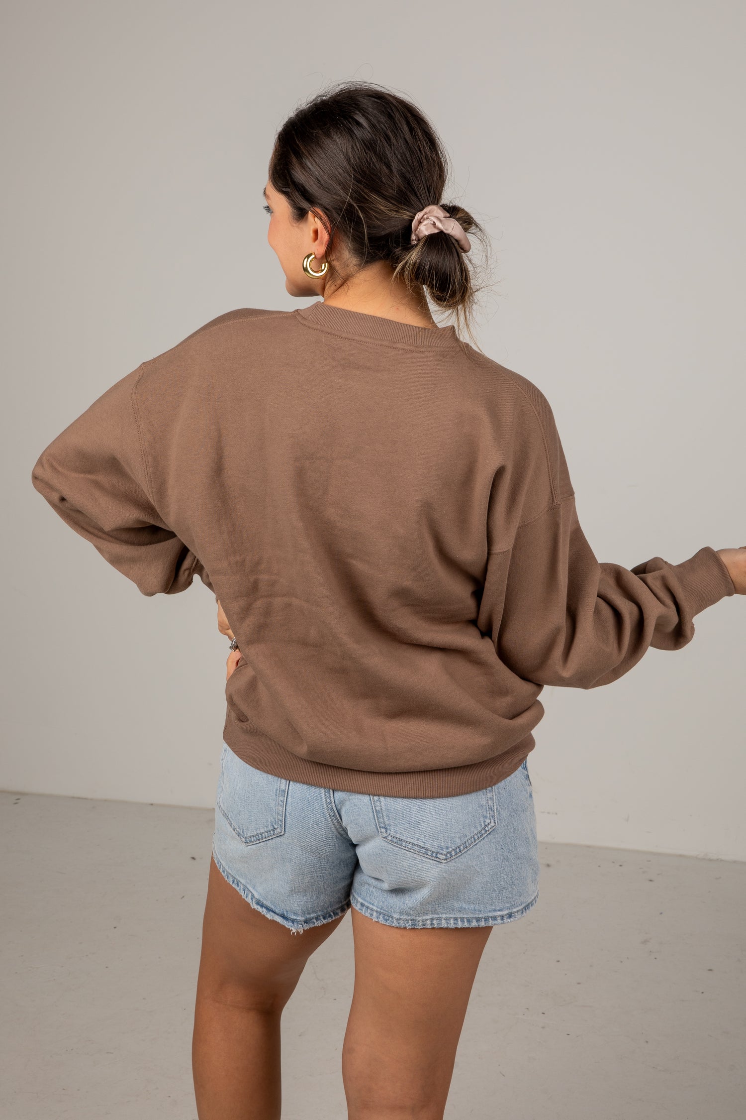 Person wearing a brown sweatshirt and denim shorts against a plain background