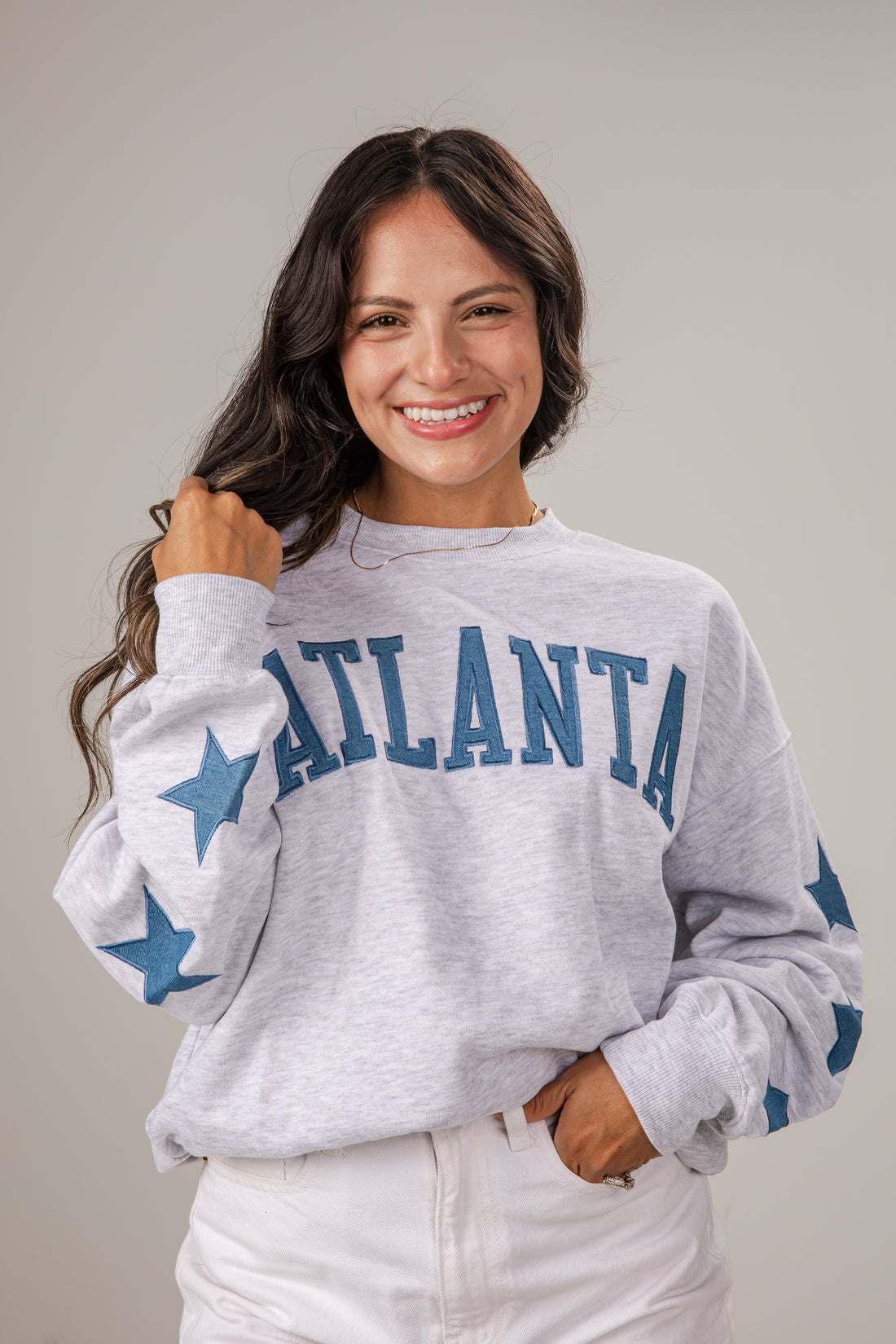 Woman wearing a gray sweatshirt with 'Atlanta' and star designs on a plain background