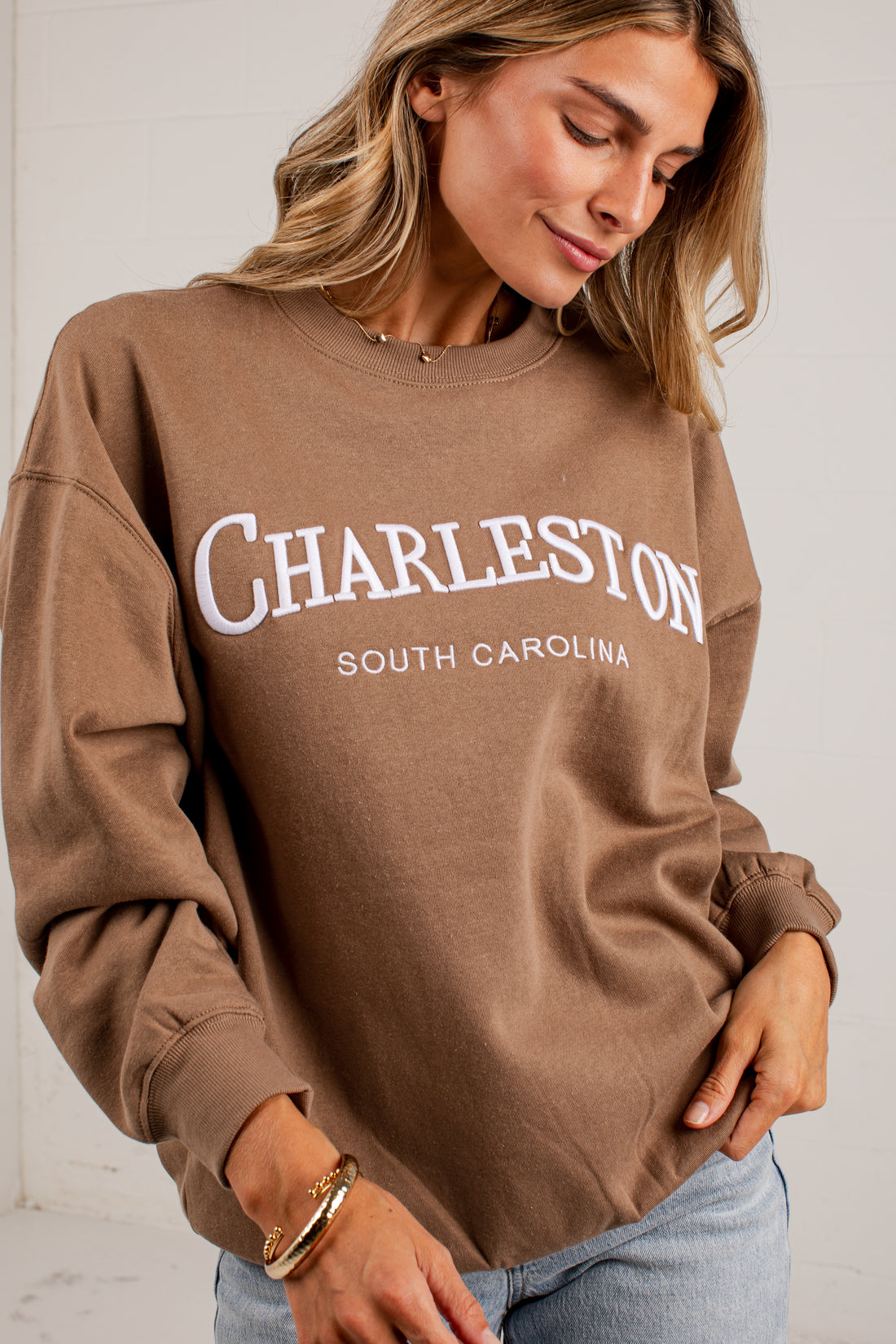 A woman wearing a brown crewneck sweatshirt with &