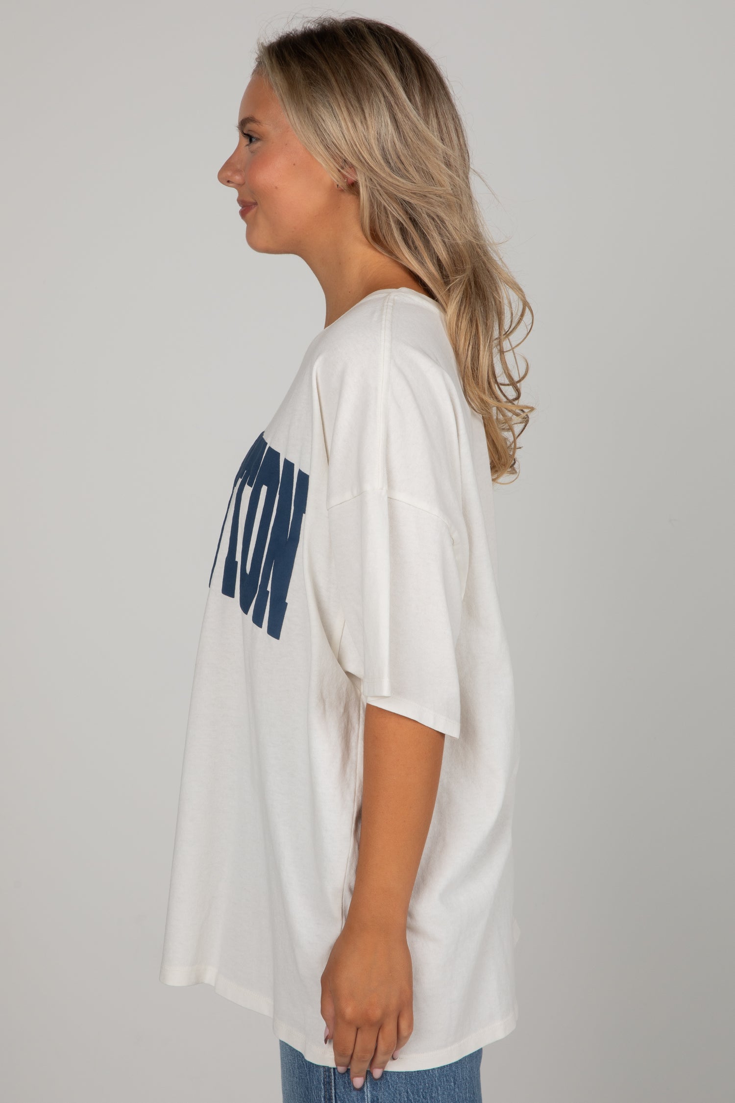Person wearing a white oversized t-shirt with blue text on a plain background