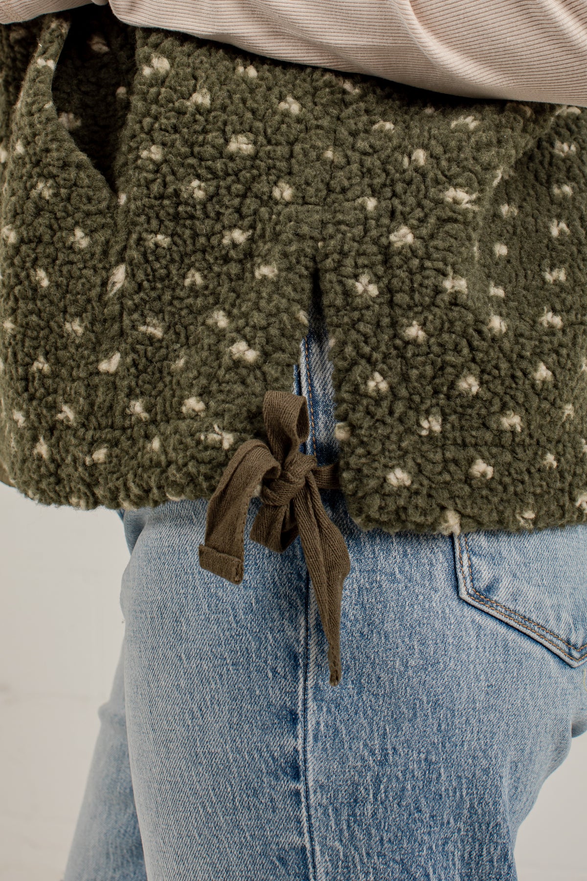 Close-up of a person wearing an olive green sherpa fleece top with small cream star details and a brown drawstring, paired with light blue jeans.