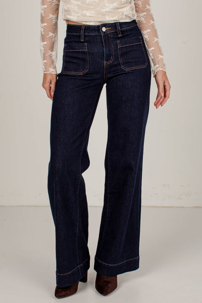 A model wearing dark blue wide-leg denim jeans with a beige lace long-sleeve top and brown suede boots, shown from the waist down against a light off-white studio background.