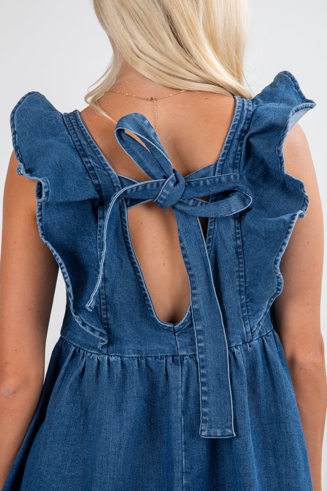 Blue denim dress with ruffled straps and open back on a plain background