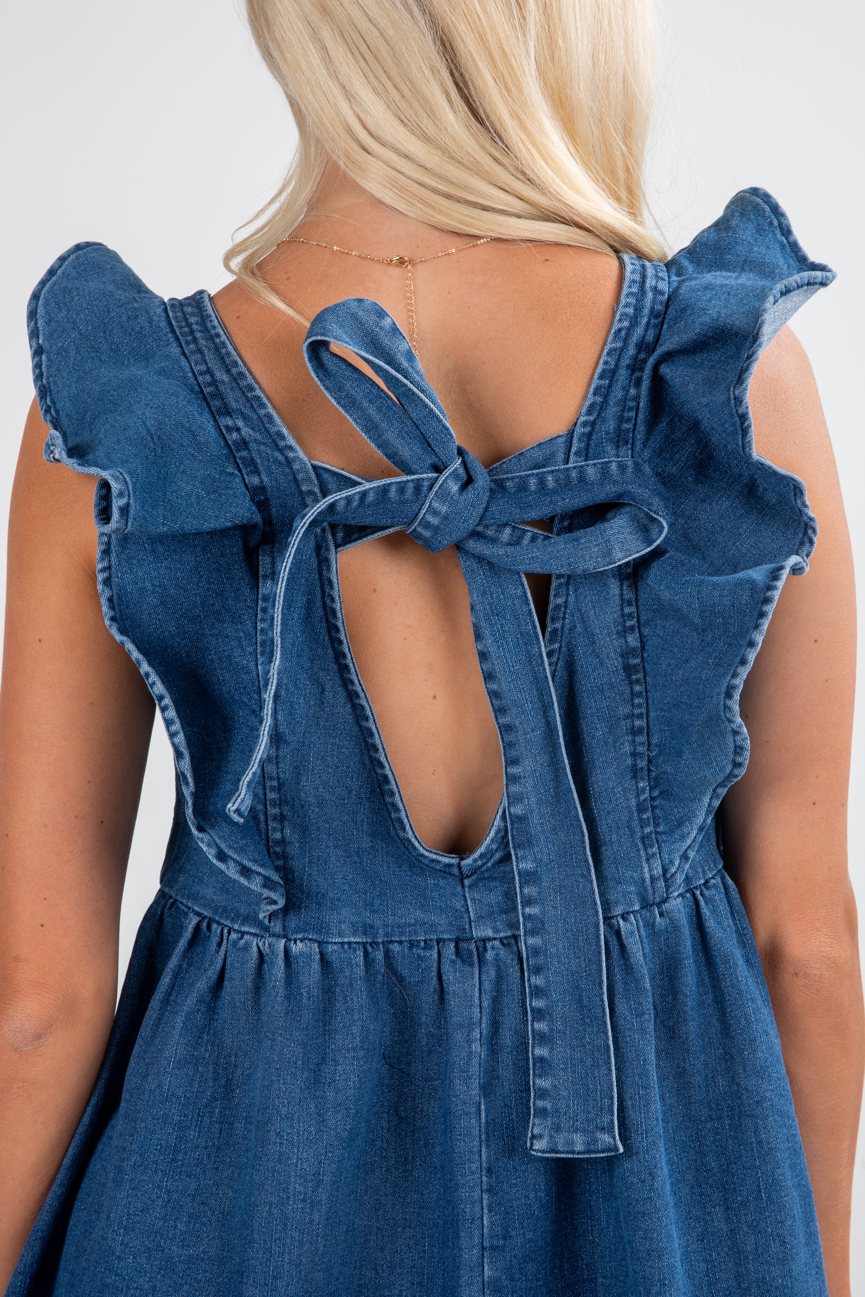 Blue denim dress with ruffled straps and open back on a plain background