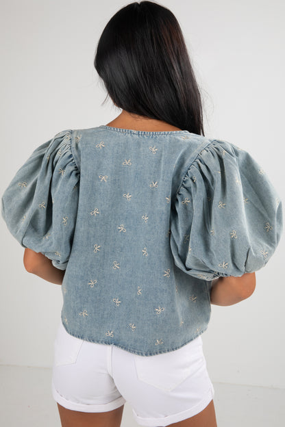 Woman wearing a light blue denim top with puff sleeves and white shorts on a plain background