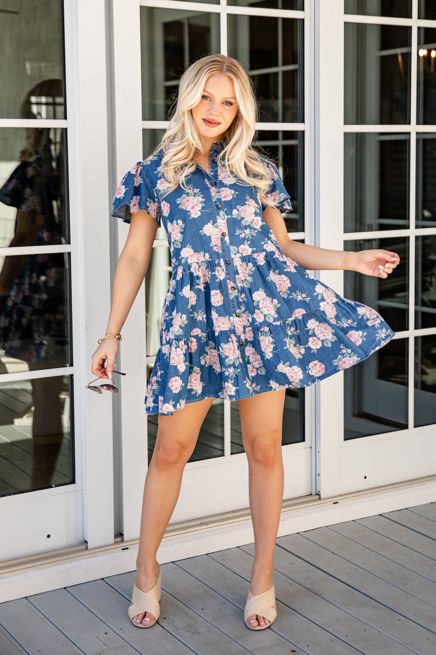 Woman in a blue floral dress standing on a wooden deck.
