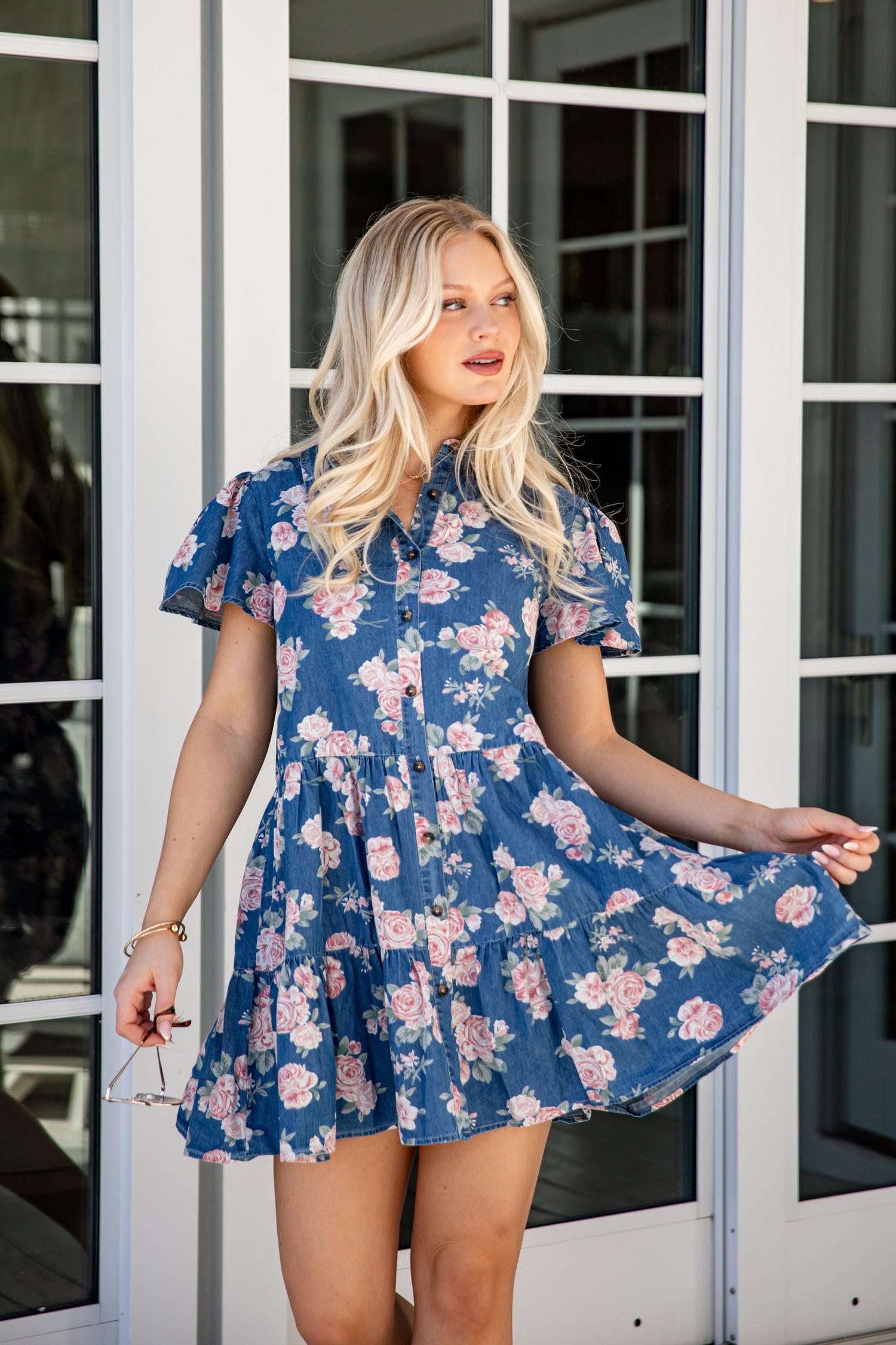 Woman wearing a blue floral dress standing in front of glass doors.