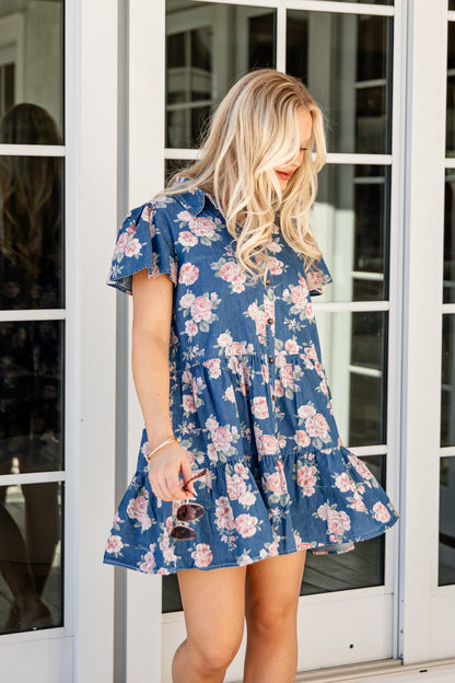 Woman wearing a blue floral dress standing in front of a glass door.