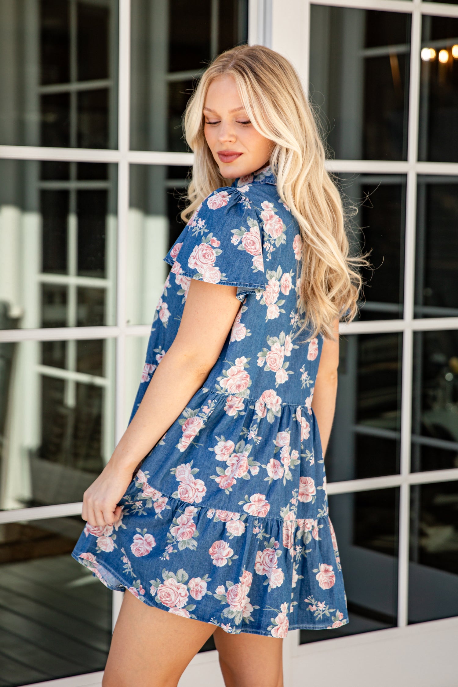 Woman wearing a blue floral dress standing in front of a glass door.