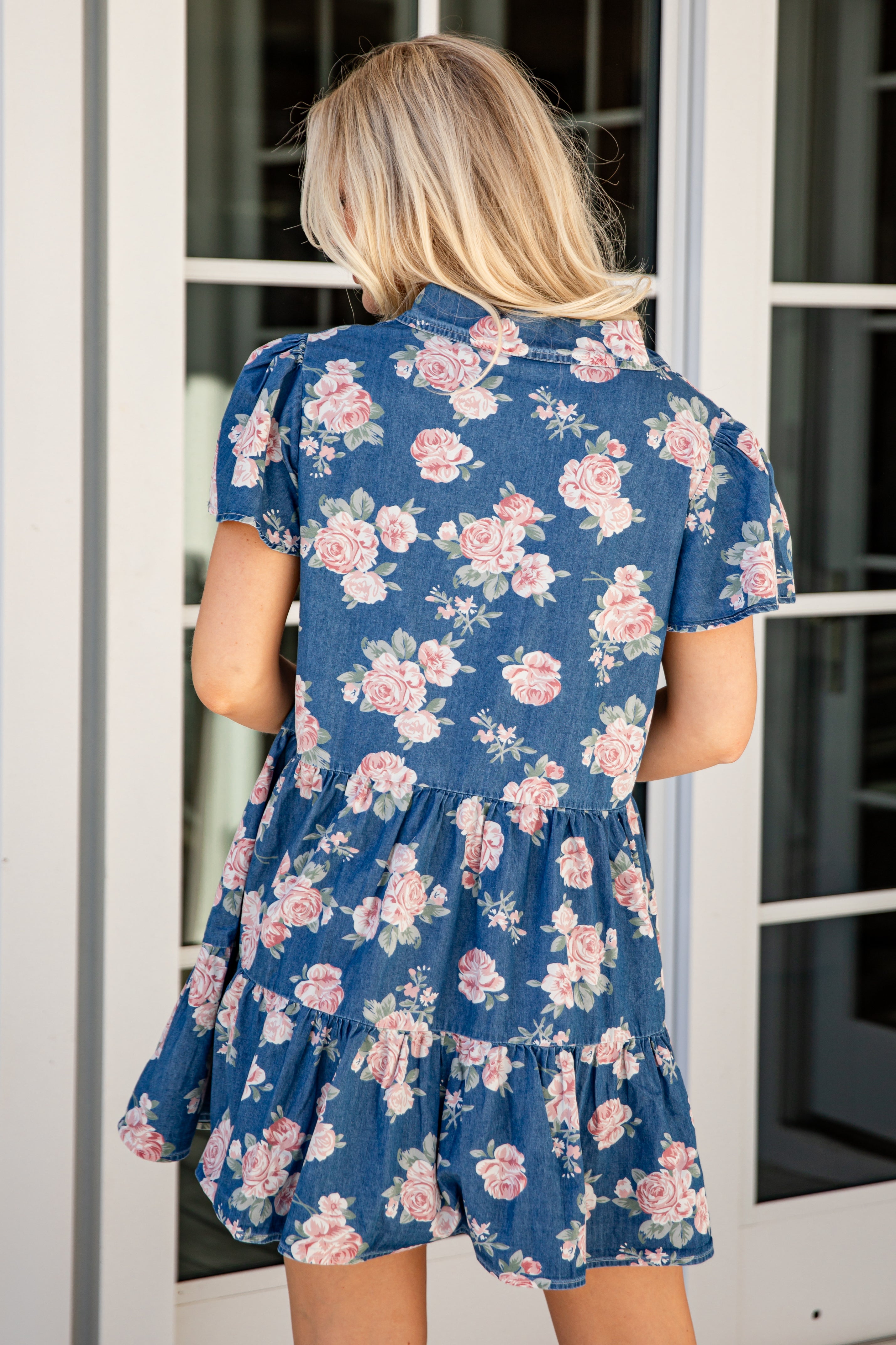 Woman wearing a blue floral dress standing in front of a white door.