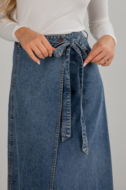 Person wearing a blue denim skirt with a white top on a plain background
