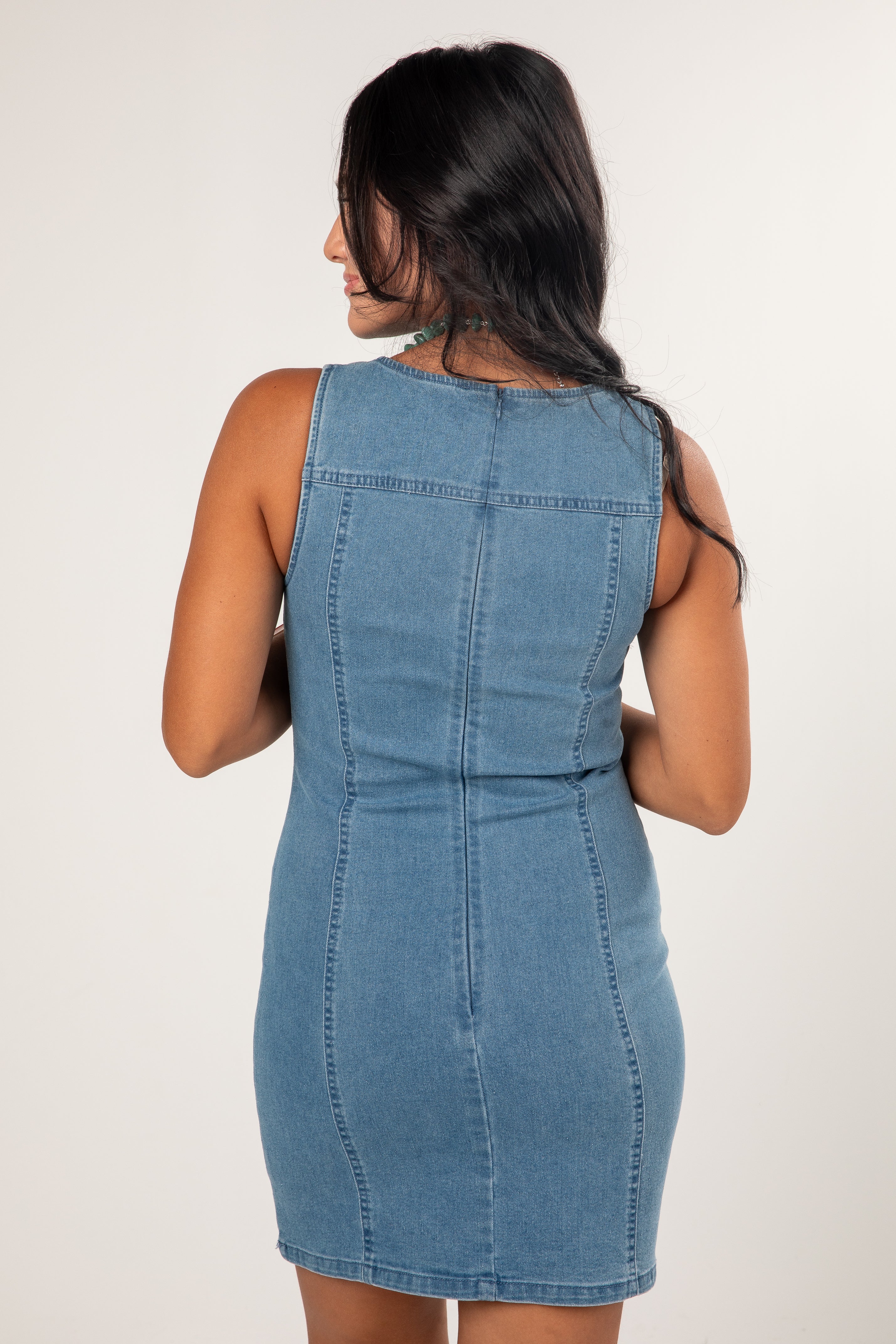 A woman shown from the back wearing a sleeveless light blue denim bodycon mini dress against a plain light background.