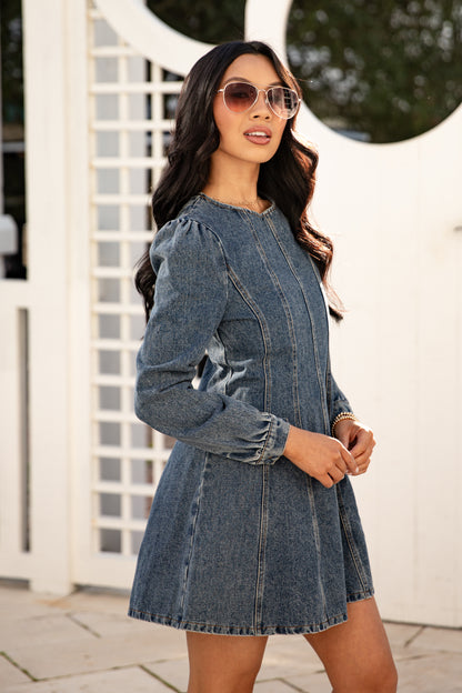 Woman wearing a denim dress with sunglasses outdoors.